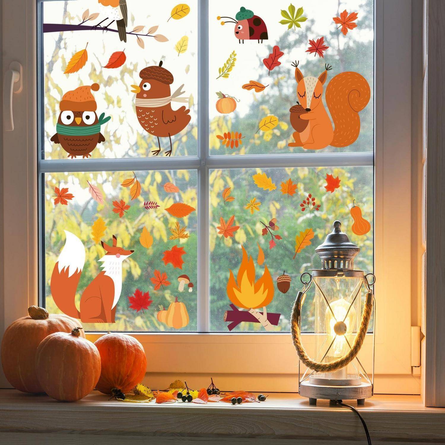 Herbstliche Fensterdekoration mit Eulen, Eichhörnchen, Fuchs, Blättern und Kürbissen, beleuchtet von einer Laterne auf einer Fensterbank mit echten Kürbissen.