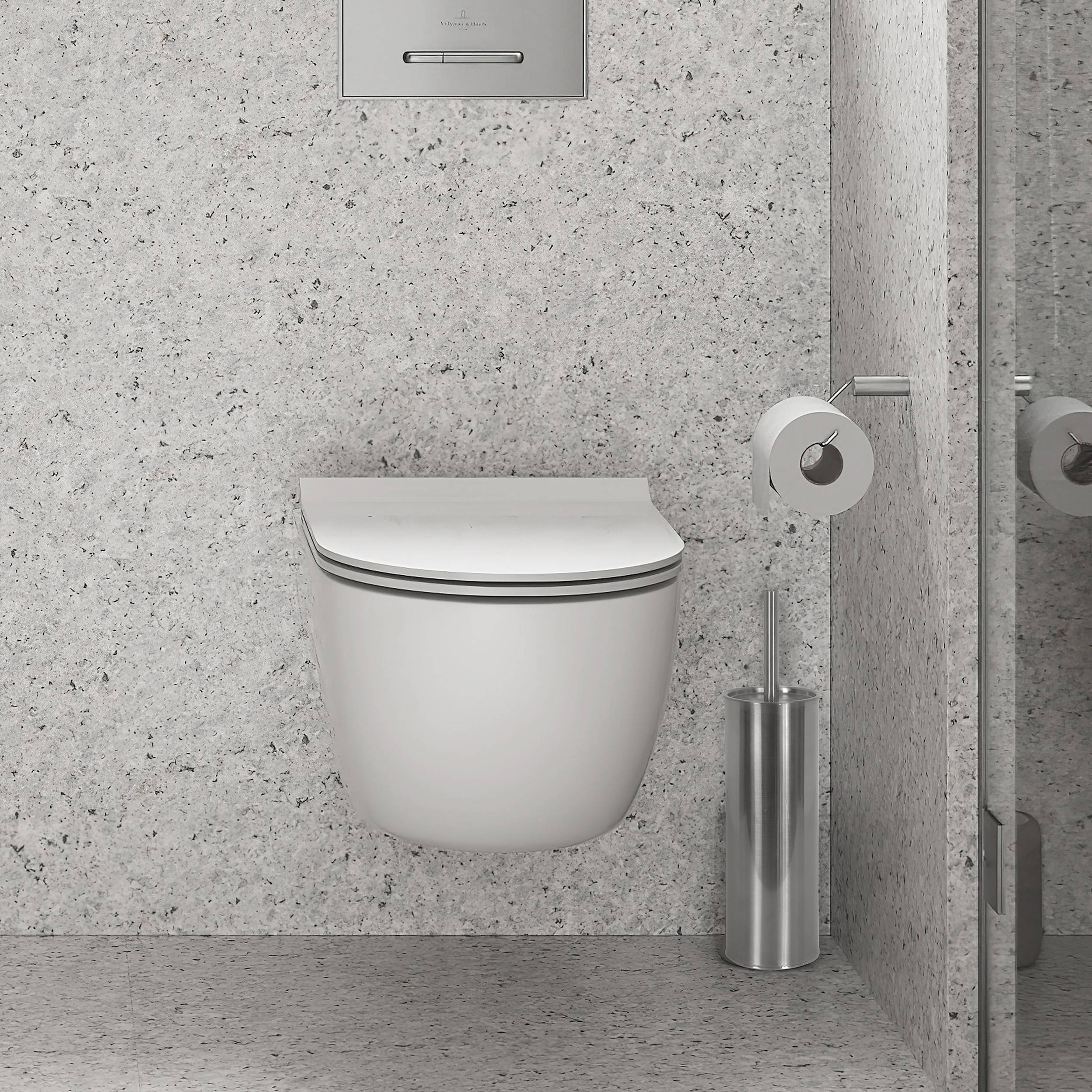 Modernes wandmontiertes Toilettenbecken mit verborgenem Spülpaneel in einem grau gefliesten Badezimmer, neben einem Toilettenpapierhalter und einer Bürstenhalterung.