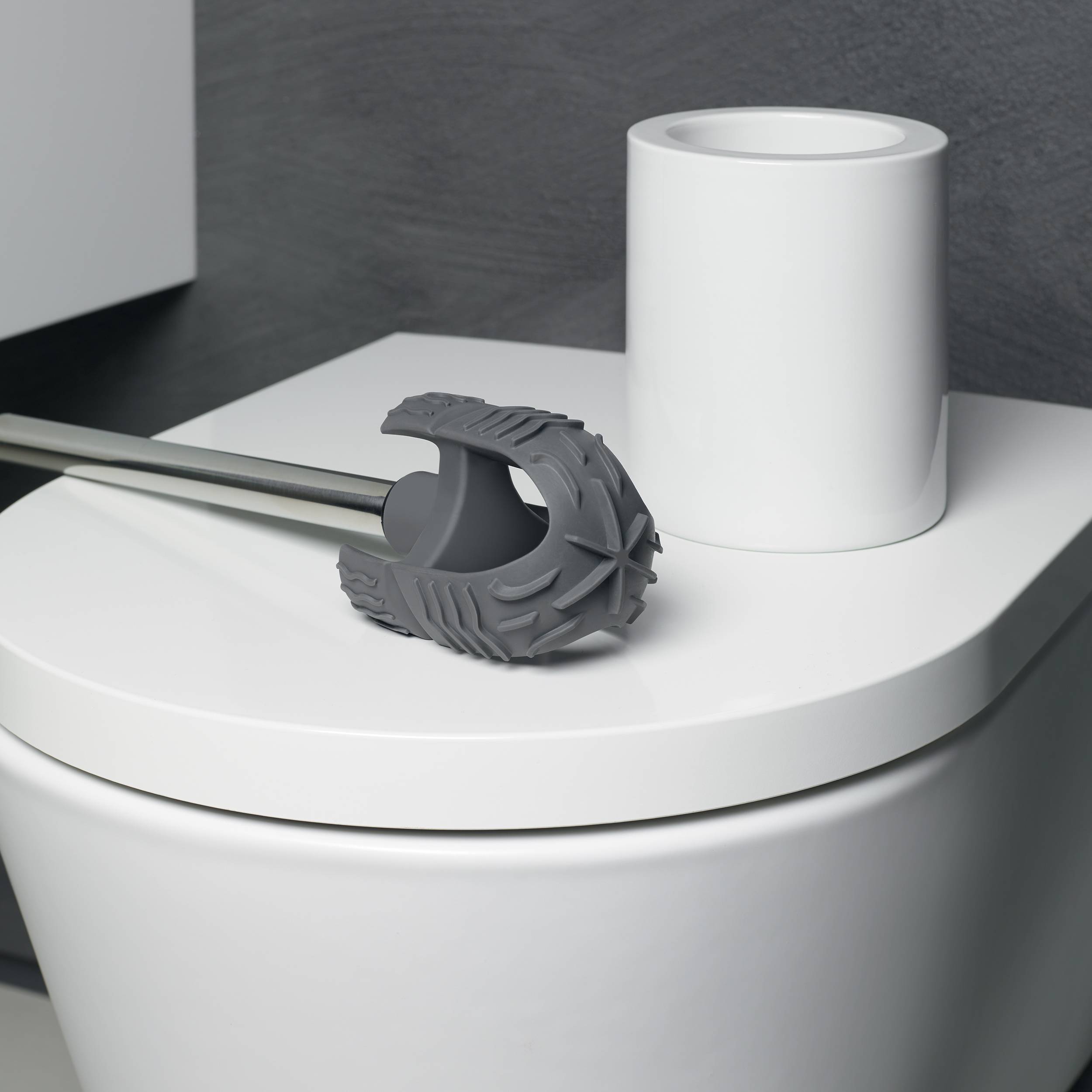 Grauer Duschablauf-Haarfänger, der an einer Metallstange neben einer weißen Badezimmerarmatur auf einem Waschbecken oder einer Arbeitsplatte befestigt ist.
