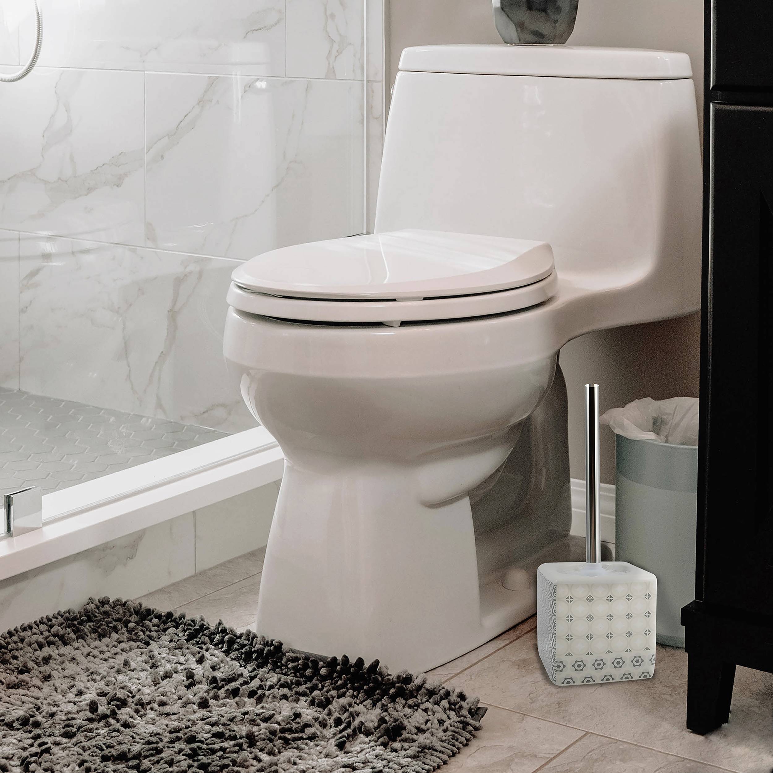 Weiße Toilette mit geschlossenem Deckel in einem modernen Badezimmer, neben einer Toilettenbürste und einem Mülleimer, mit einer Badewanne und gefliesten Wänden in der Nähe.