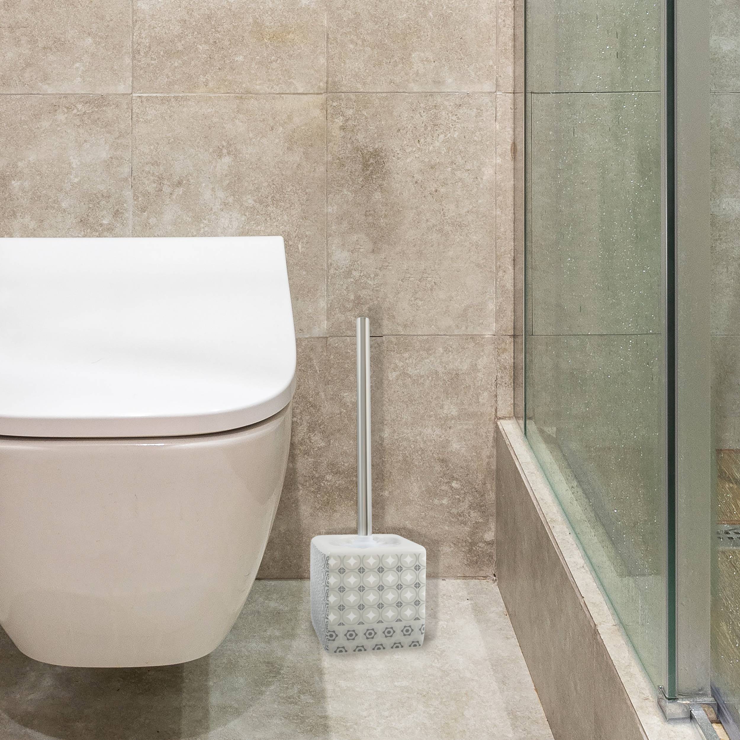 Modernes Badezimmer mit einer wandmontierten Toilette und einer Toilettenbürste neben einer Glasduschwand auf beigefarbenen Fliesenboden und Wänden.