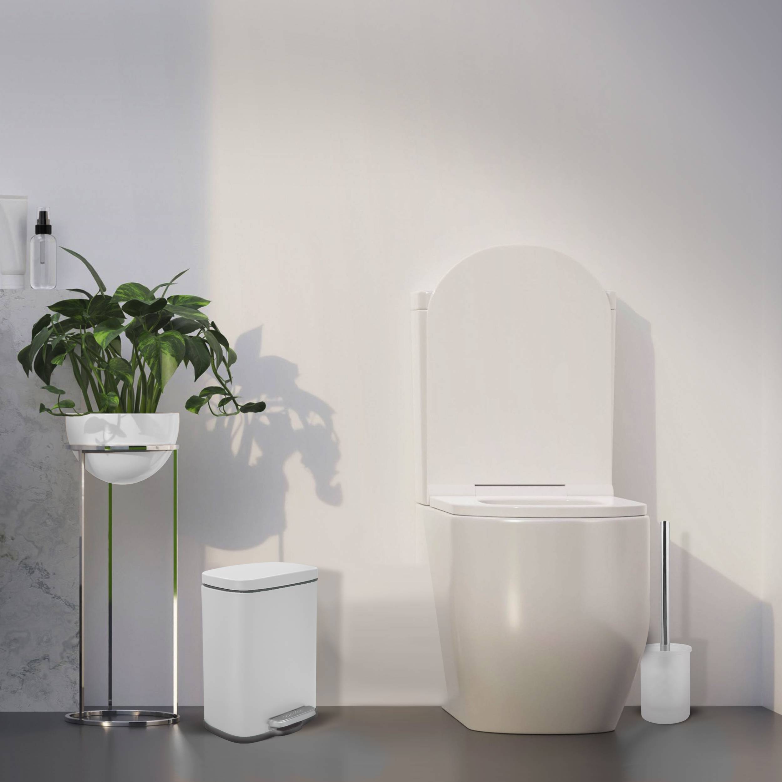 Minimales modernes Badezimmer mit einer weißen Toilette, kleinem Mülleimer, Toilettenbürsenhalter und einer Topfpflanze auf einem Ständer vor einer schlichten Wand.