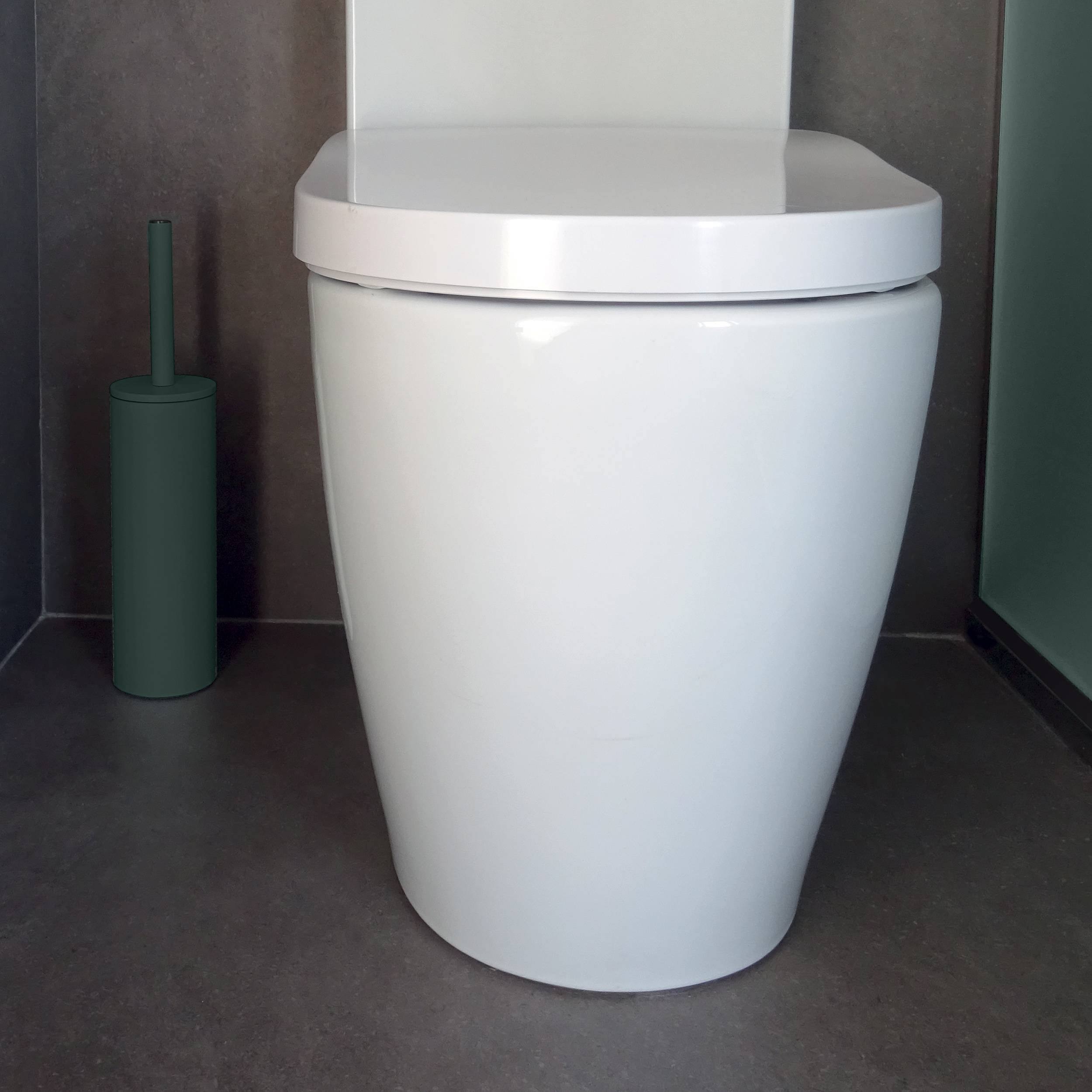 Modernes weißes Toilettenbecken in einem dunkel gefliesten Badezimmer mit einem grünen Toilettenbürsten-Halter daneben.