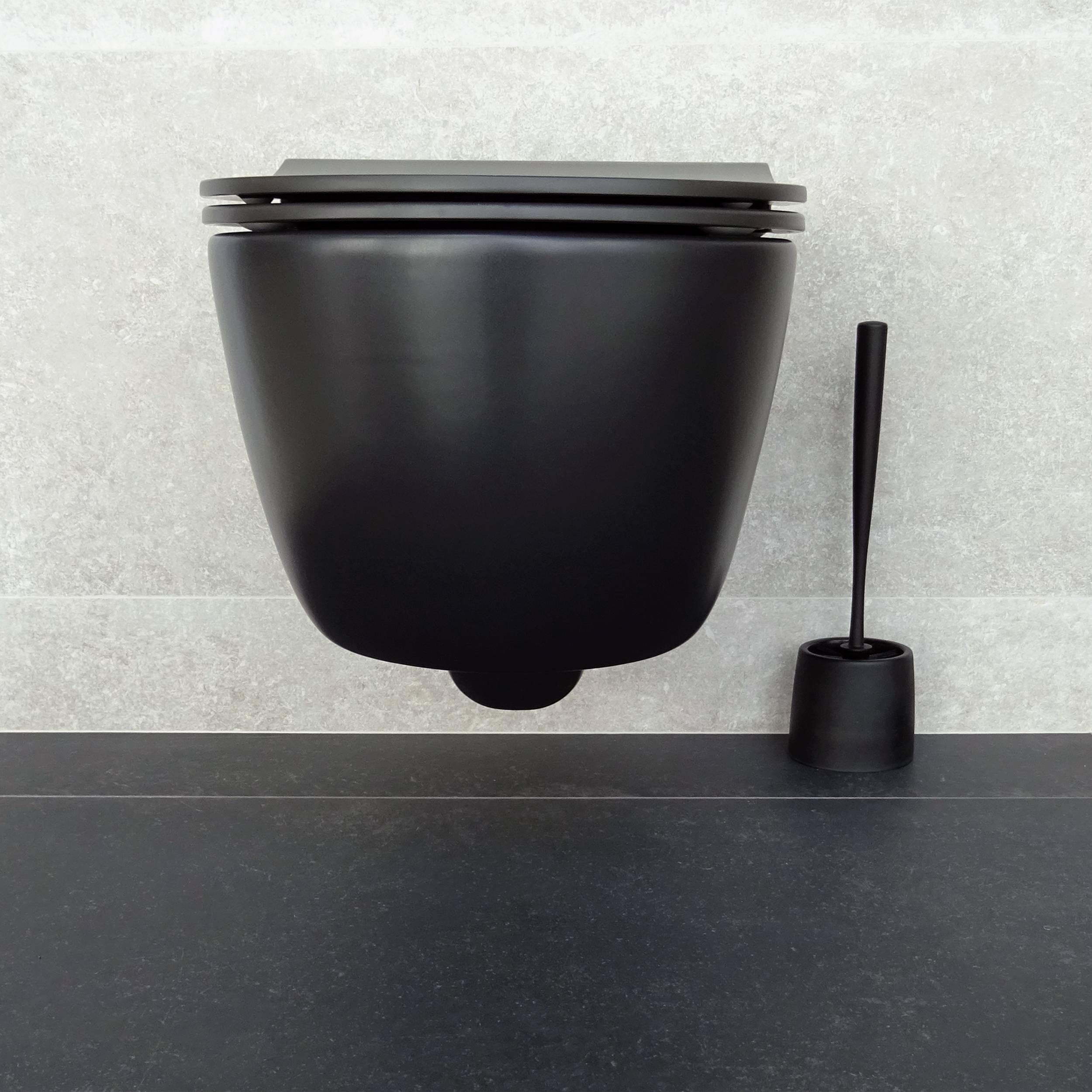 Schwarze wandmontierte Toilette mit passendem Toilettenbürstenhalter auf einer dunklen Arbeitsplatte vor einer hellen gefliesten Wand.