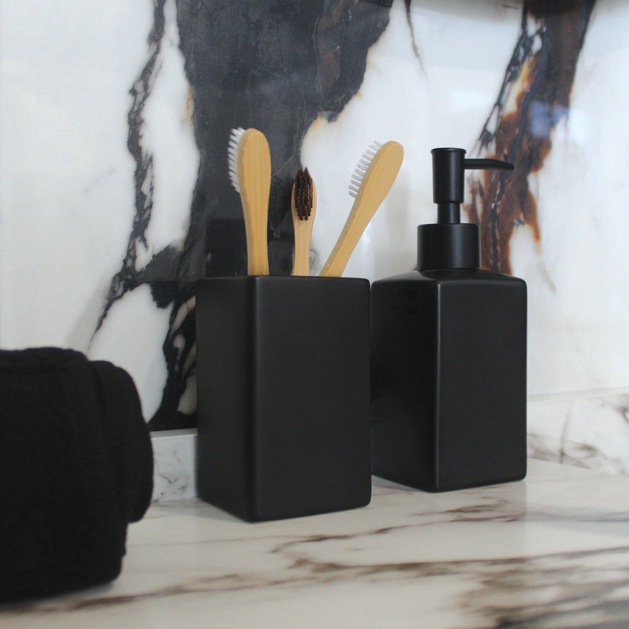 Schwarzes Badezimmer-Ablagewaschset mit Seifenspender, Zahnbürstenhalter und gefalteten Handtüchern vor einer Marmor-Wandfläche.