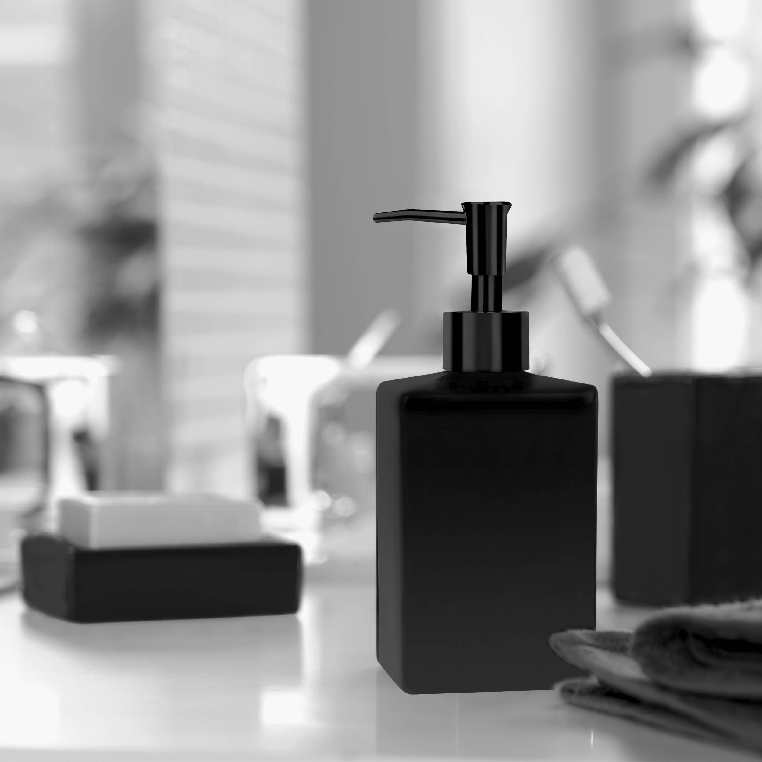 Schwarze Pumpen-Seifenspender auf einer Badezimmerablagefläche, mit Handtüchern und Toilettenartikeln im unscharfen Hintergrund.
