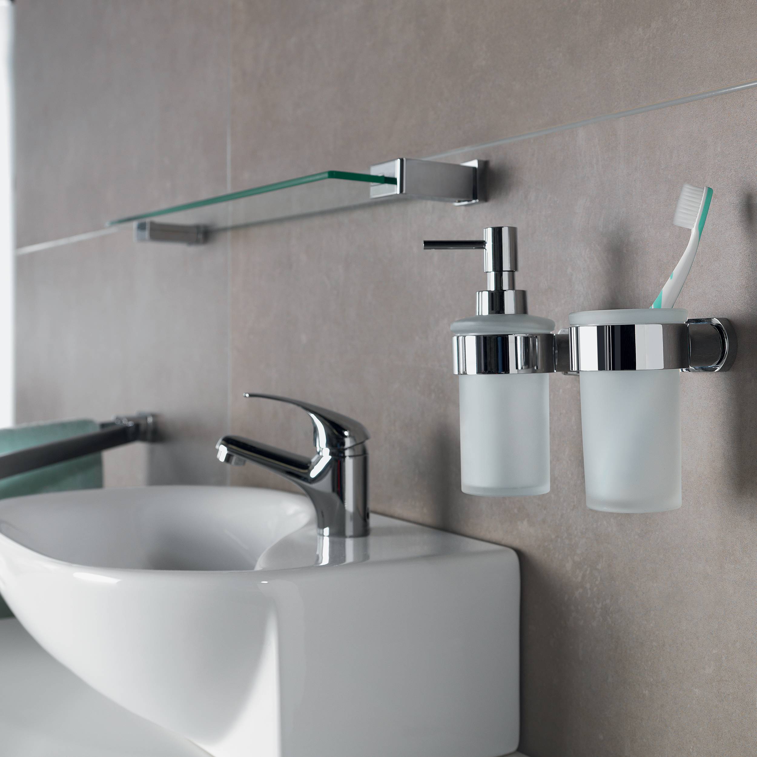 Modernes Badezimmerbecken mit Chromarmatur, Glasregal und wandmontiertem Seifenspender und Zahnbürstenhalter neben einem weißen Waschbecken.