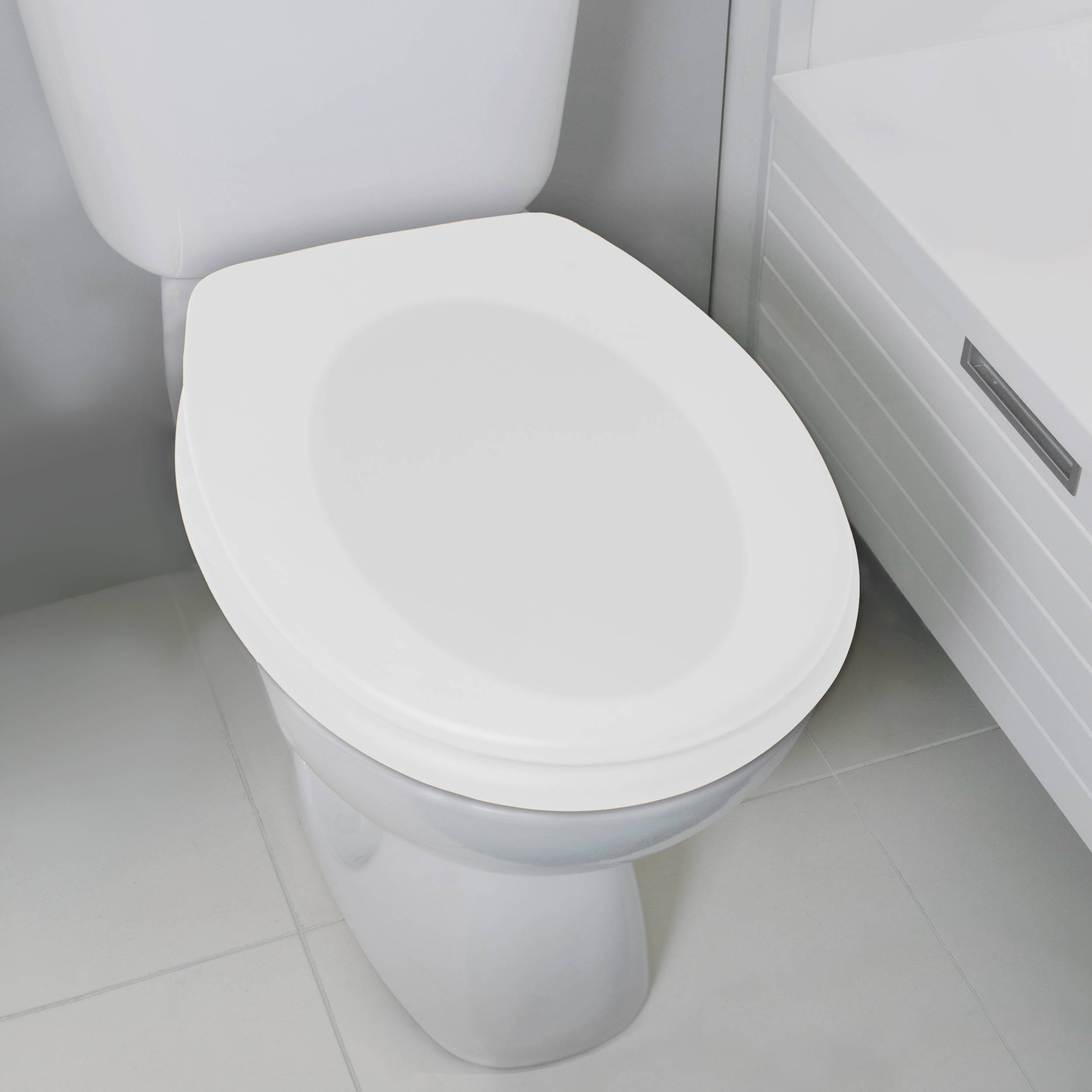 Weiße Toilette mit geschlossenem Sitz und Deckel, von oben betrachtet in einer Badezimmerecke mit hellgrauem Fliesenbelag und einem Schrank daneben.