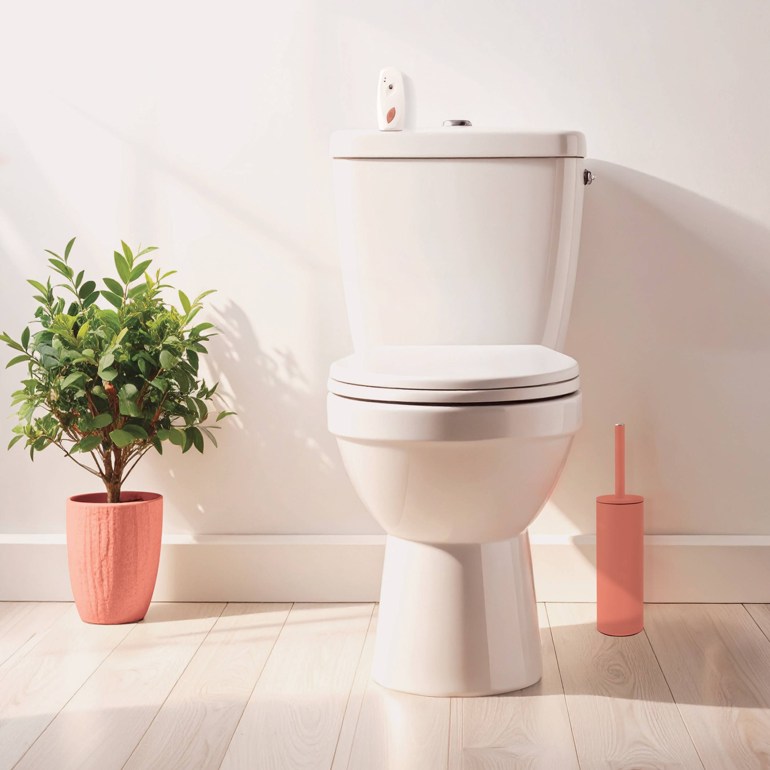 Weiße Toilette in einem hellen, minimalistischen Badezimmer, mit einer Topfpflanze auf der linken Seite und einer rosa Toilettenbürste auf der rechten Seite.
