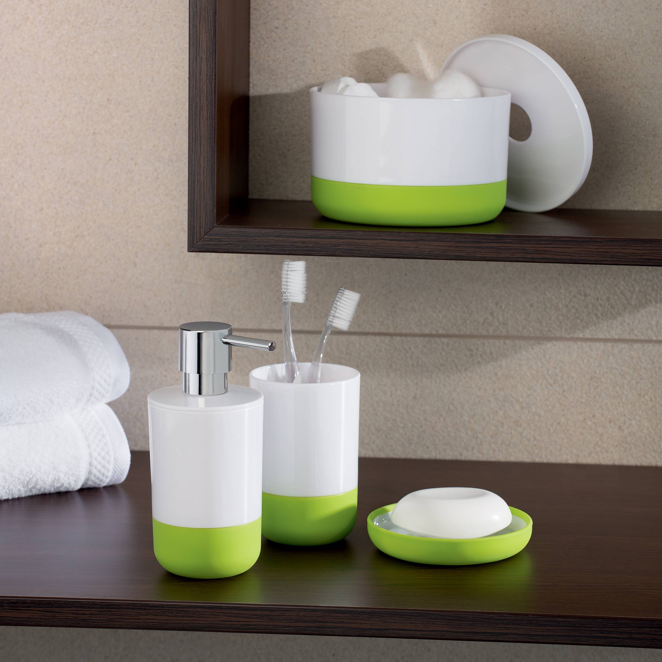 Badezimmer-Arbeitsplatte mit weißem und grünem Seifenspender, Zahnbürstenbecher, Seifenschale, gerollten Handtüchern und einem passenden Aufbewahrungsbehälter auf einem Regal.