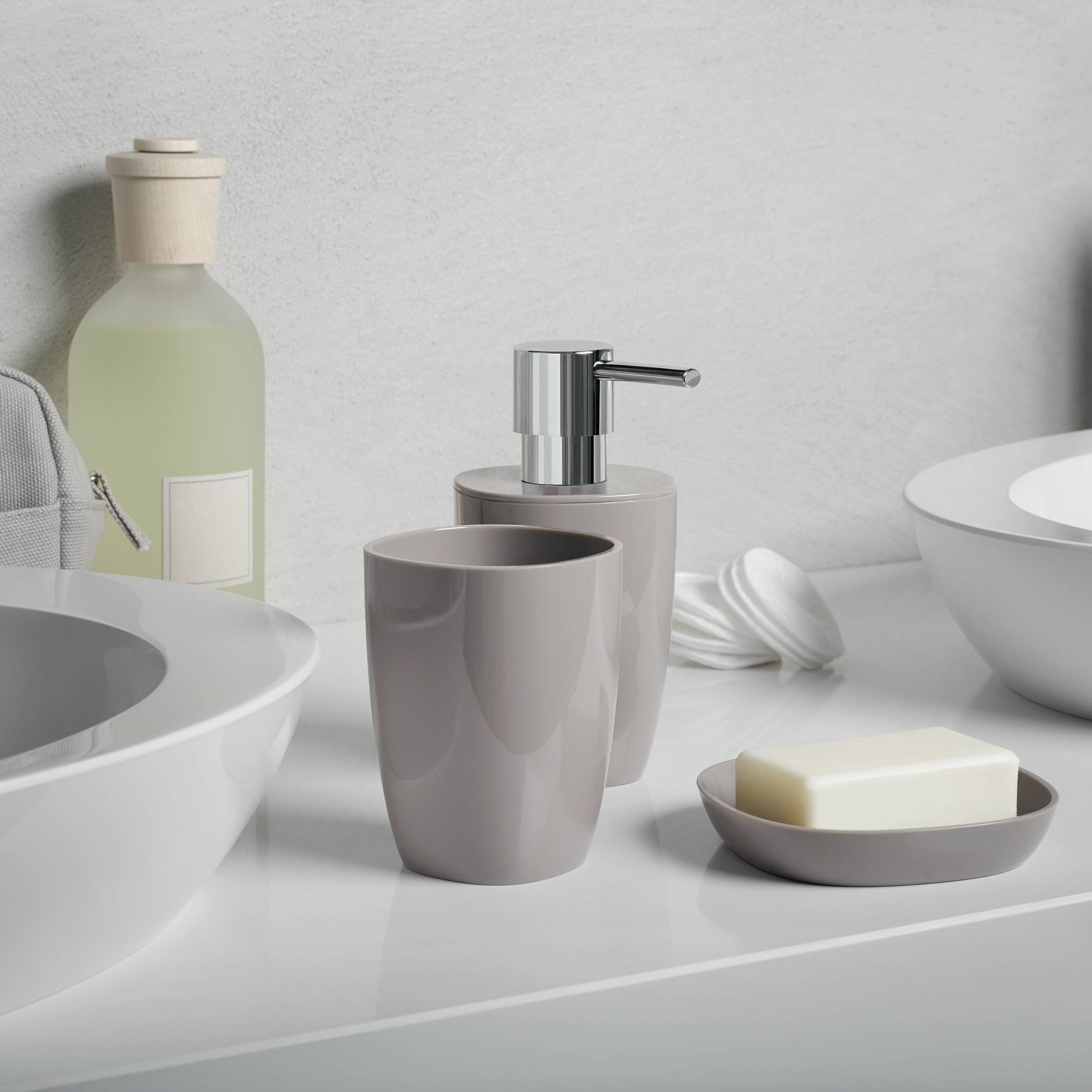 Minimalistische Badezimmerablage mit Waschbecken, Seifenspender, Becher, Seifenschale und gefalteten Handtüchern in neutralen Tönen.