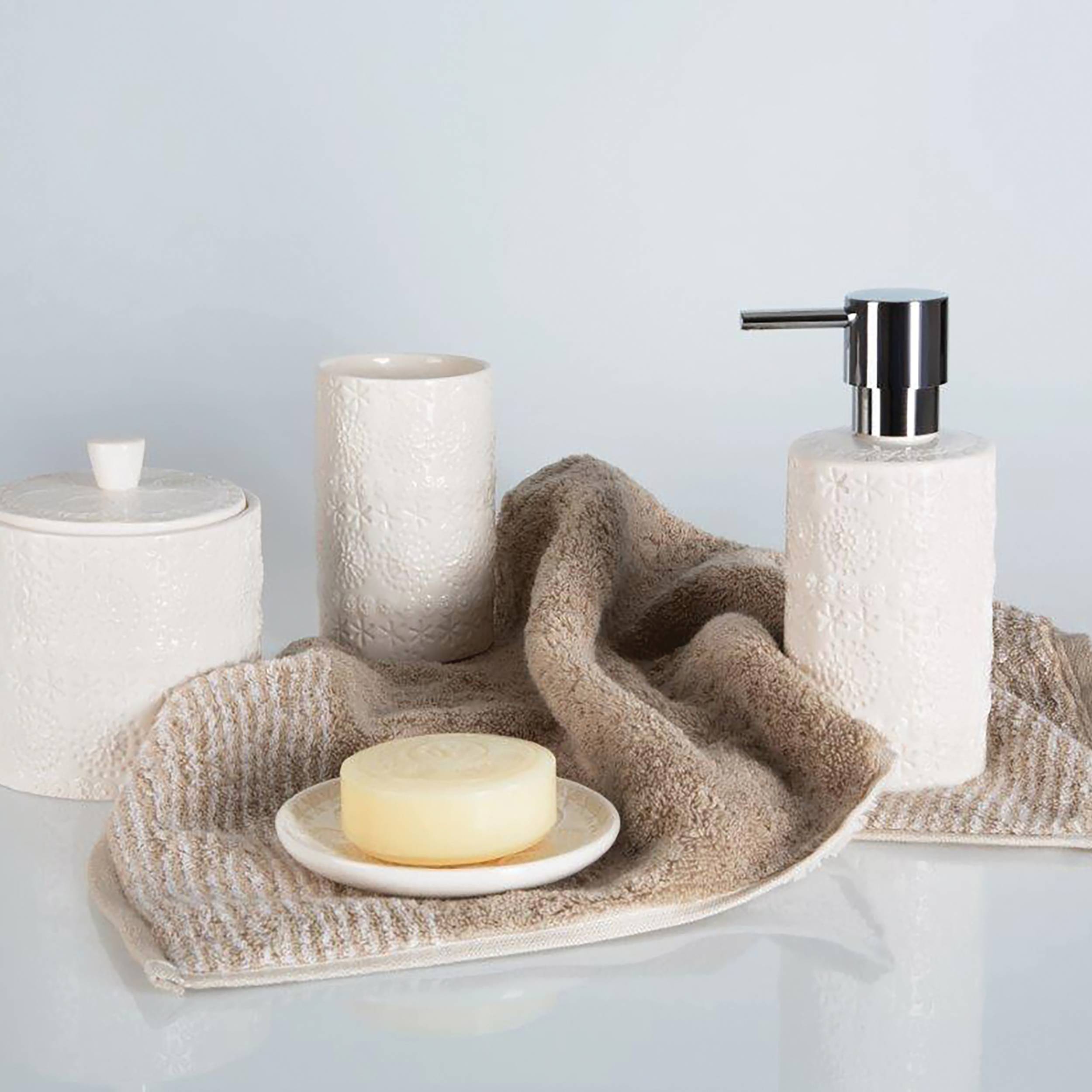 Spa-ähnliches Badezimmerset mit strukturiertem weißem Handtuch, Seifenschale und Seife, Behälter mit Deckel, Tasse und Lotionsspender auf einer neutralen Oberfläche angeordnet.