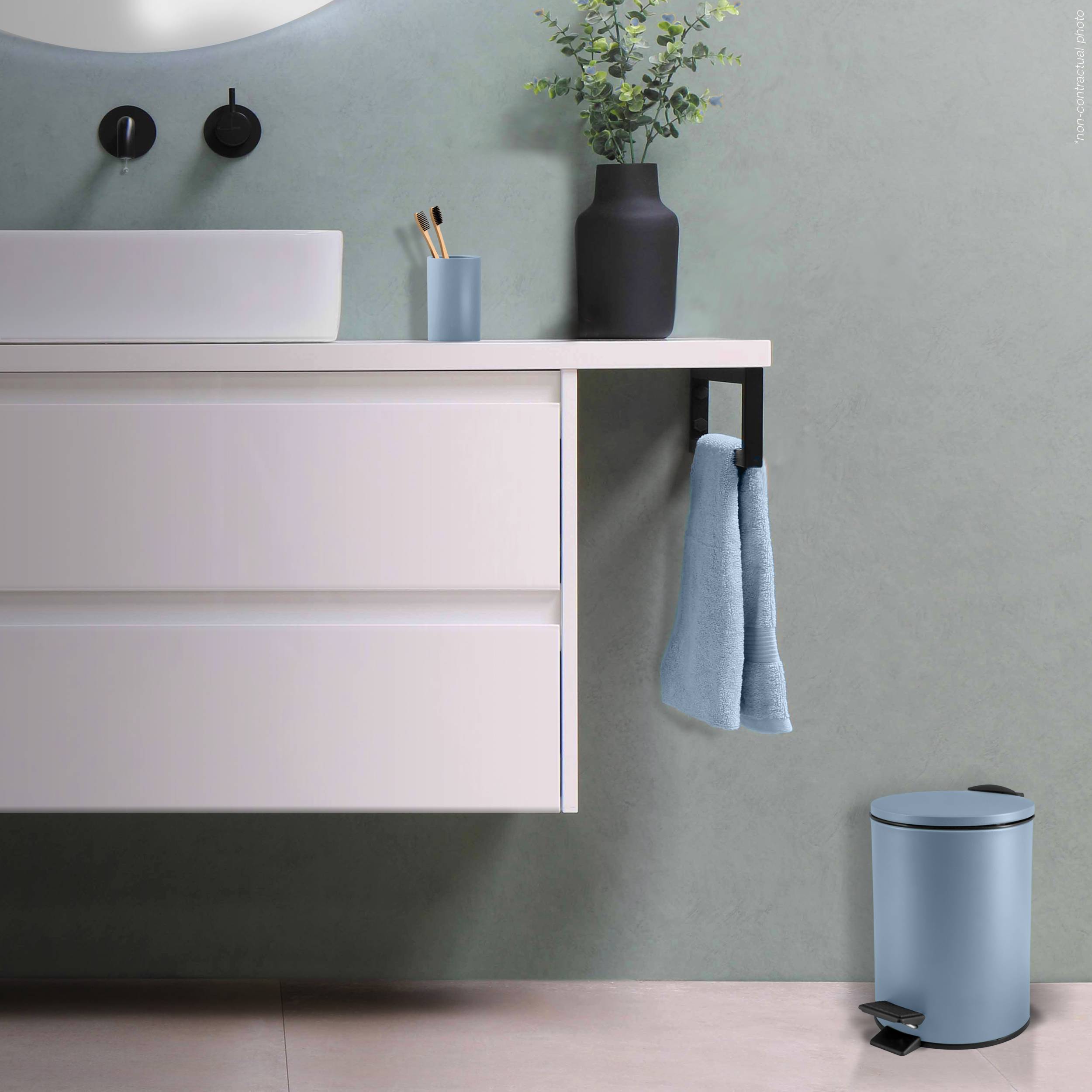 Modernes Badezimmer mit einem weißen schwebendem Waschtisch, wandmontiertem Waschbecken und schwarzem Wasserhahn, einem Handtuch, das über der Arbeitsplatte hängt, und einem blauen Mülleimer mit Deckel auf dem Boden.