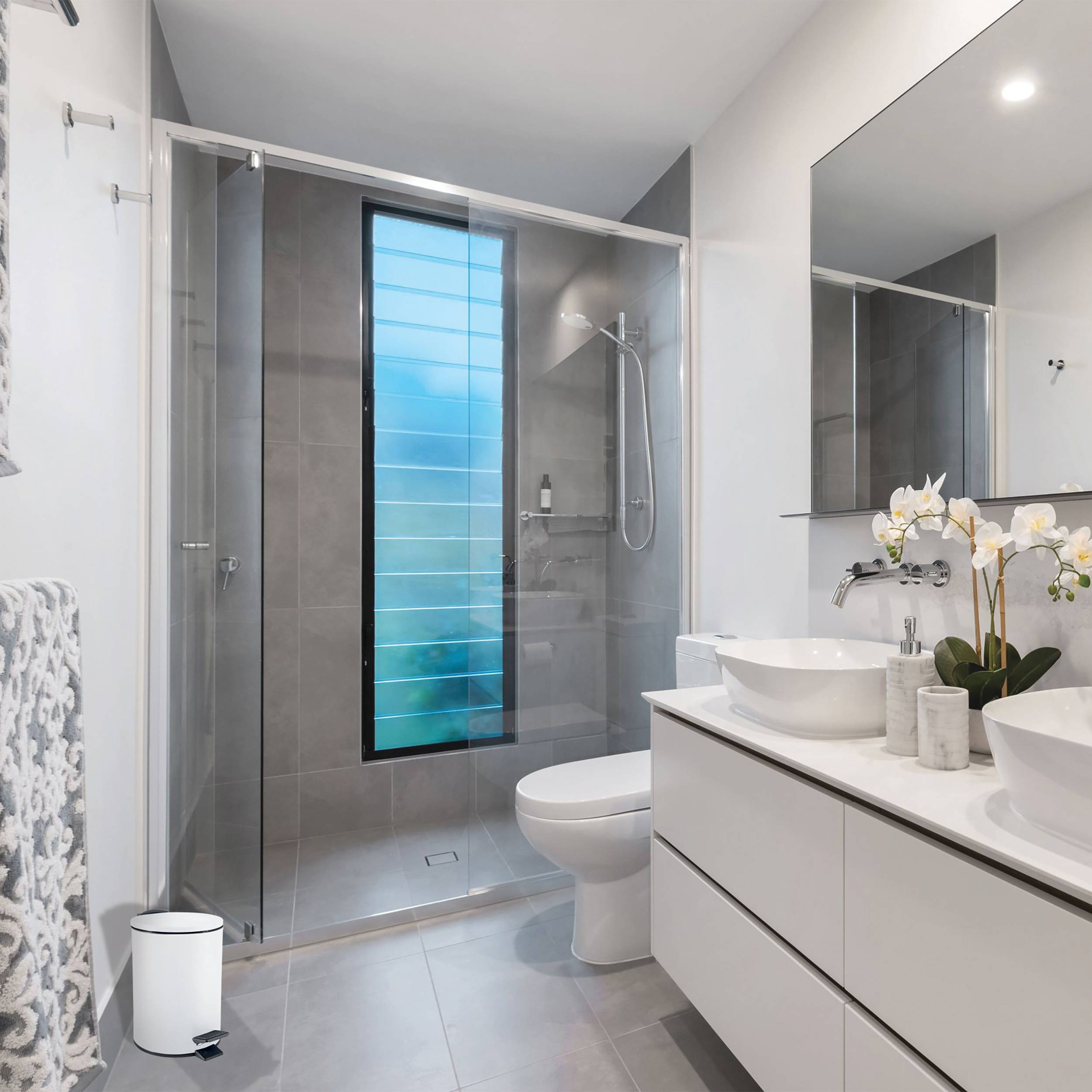 Modernes Badezimmer mit Glasduschkabine, Toilette, Doppelwaschtisch, großem Spiegel und mattblauem Fenster.