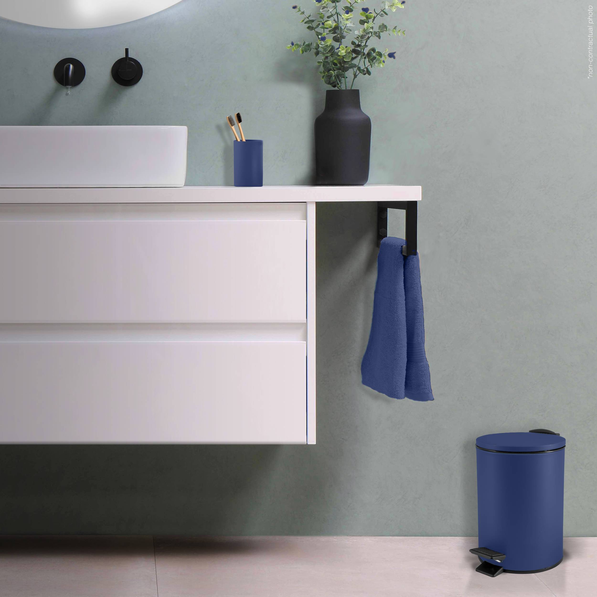 Modernes Badezimmerwaschtisch mit weißem Spülenschrank, blauem Handtuch, das über der Theke hängt, Vase und Zahnbürstenhalter oben drauf und einem blauen Mülleimer auf dem Boden.