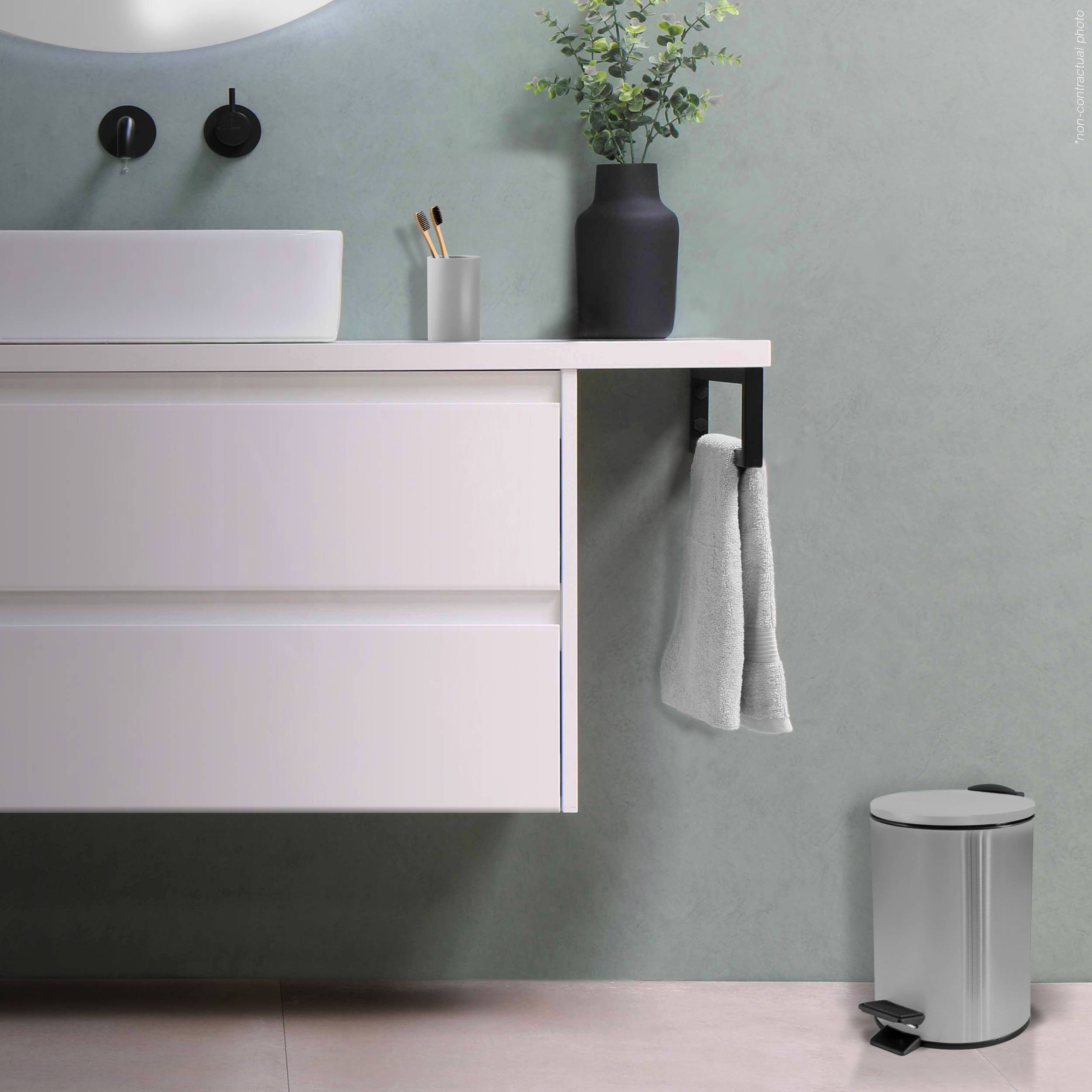 Modernes Badezimmer mit schwebendem weißen Waschtisch, wandmontagiertem Waschbecken und Wasserhahn, schwarzer Vase mit Pflanze, Handtüchern an seitlichem Haken und silbernem Mülleimer.