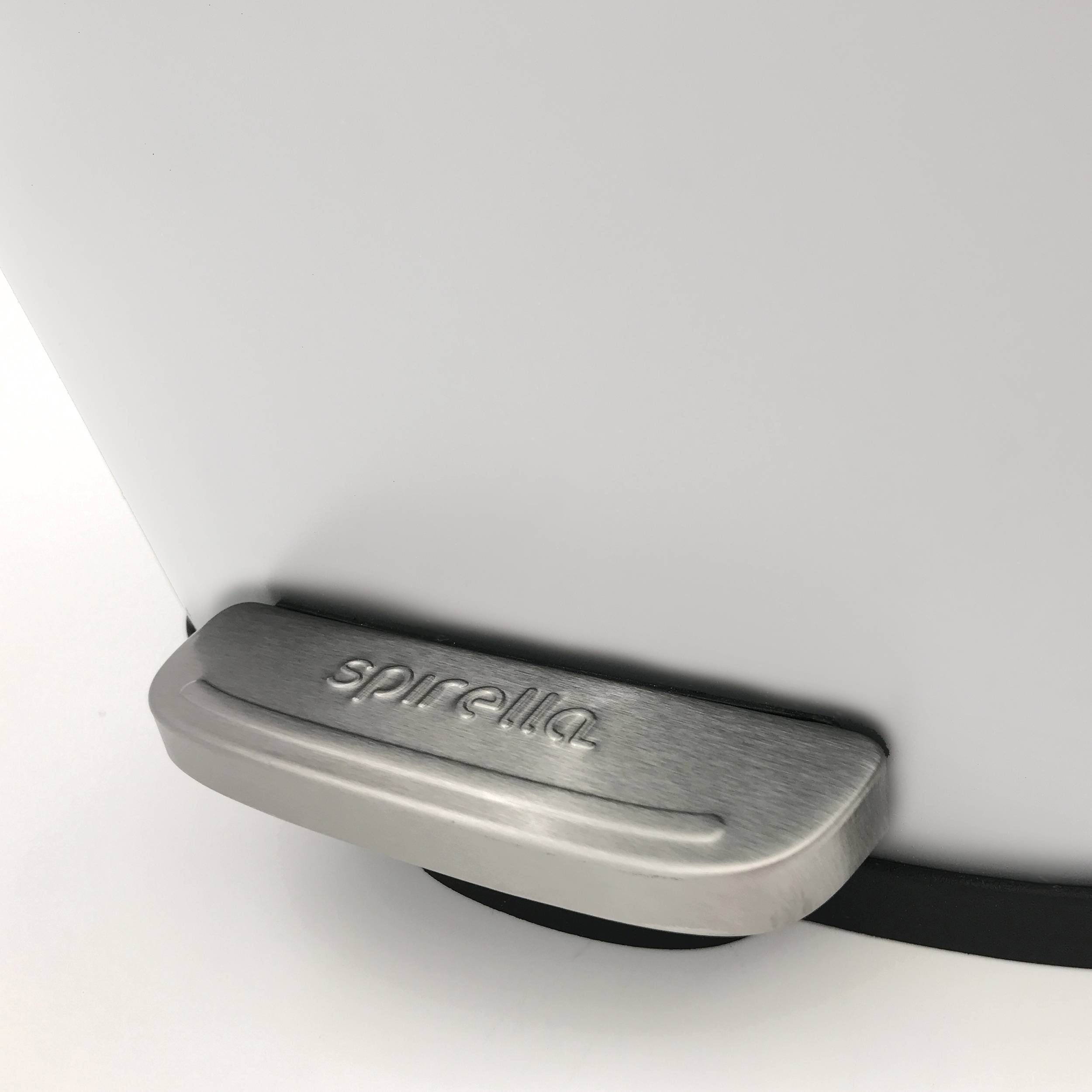 Nahaufnahme eines gebürsteten Metallgriffs mit 'spirella'-Deckel auf einem weißen Behälter oder Toilettensitz.