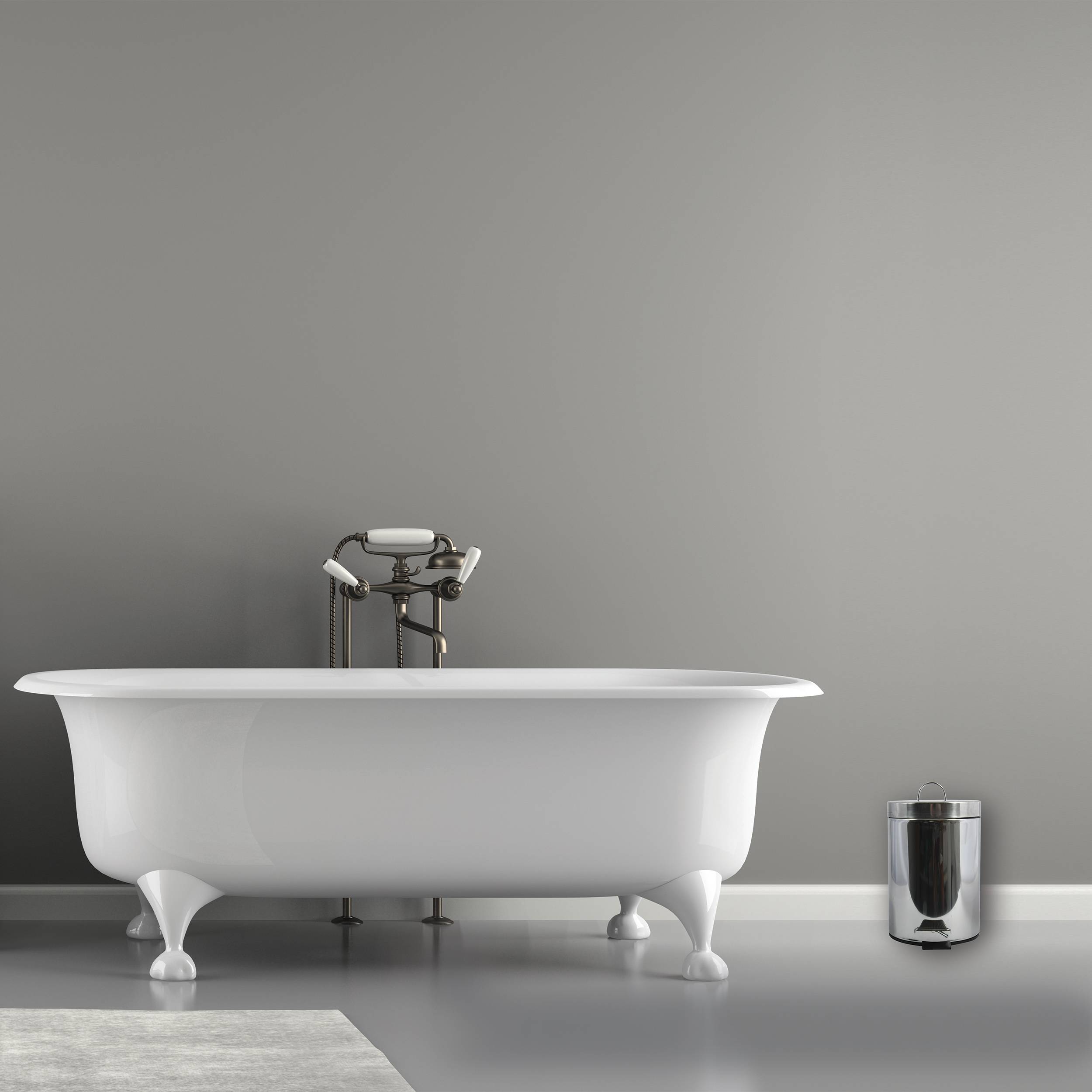 Freistehende weiße Badewanne mit Klauen auf Füßen und sichtbaren Rohren vor einer grauen Wand, mit einem kleinen Metallmülleimer daneben auf einem minimalistischen Badezimmerboden.