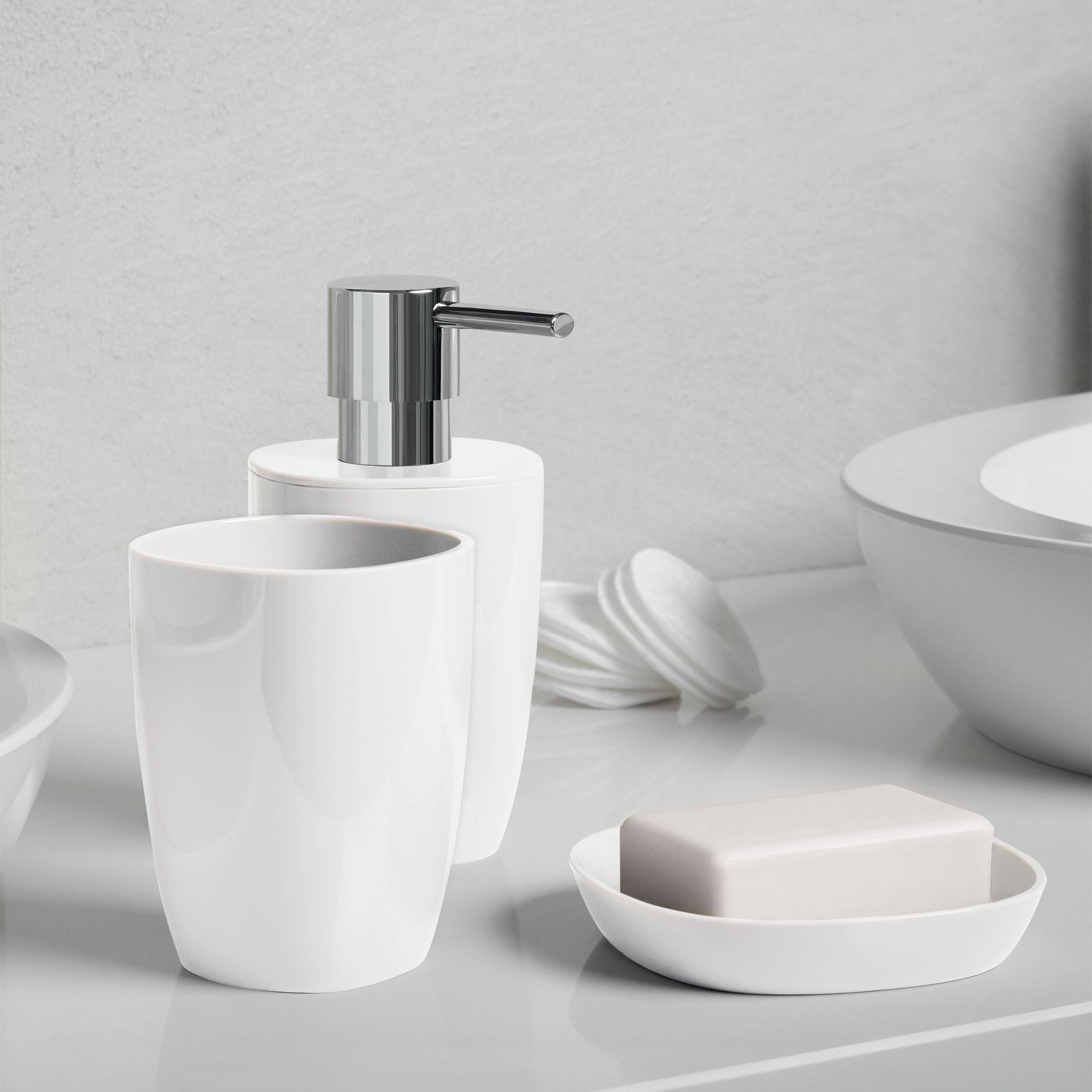 Badezimmertheke mit weißer Keramiktasse, Seifenspender, Seifenschale mit Stückseife und Schüssel auf einer sauberen grauen Oberfläche.