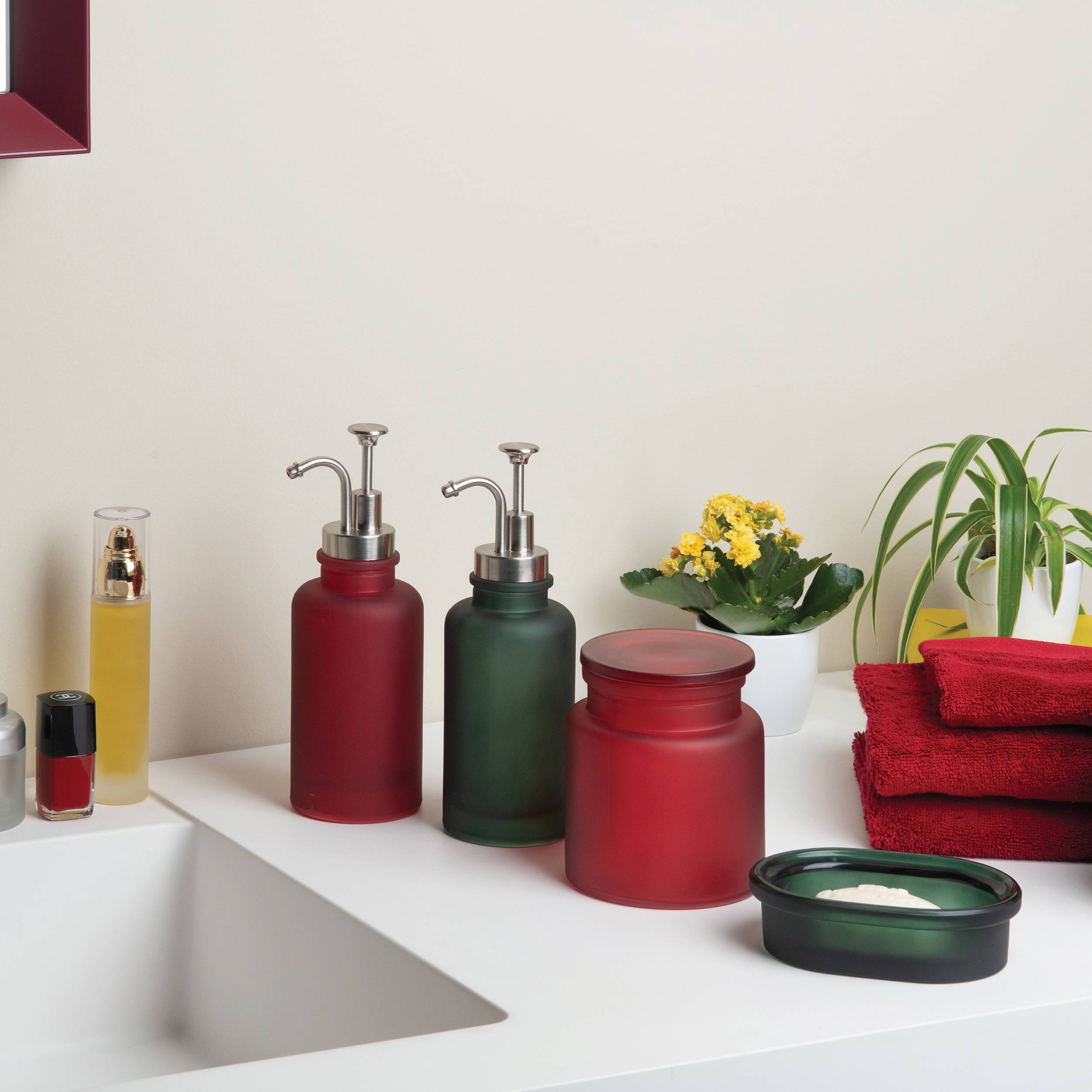Badezimmer-Arbeitsplatte mit zwei Seifenspendern, einem Glas, Handtüchern, einer Topfpflanze und einem Waschbecken auf der linken Seite.