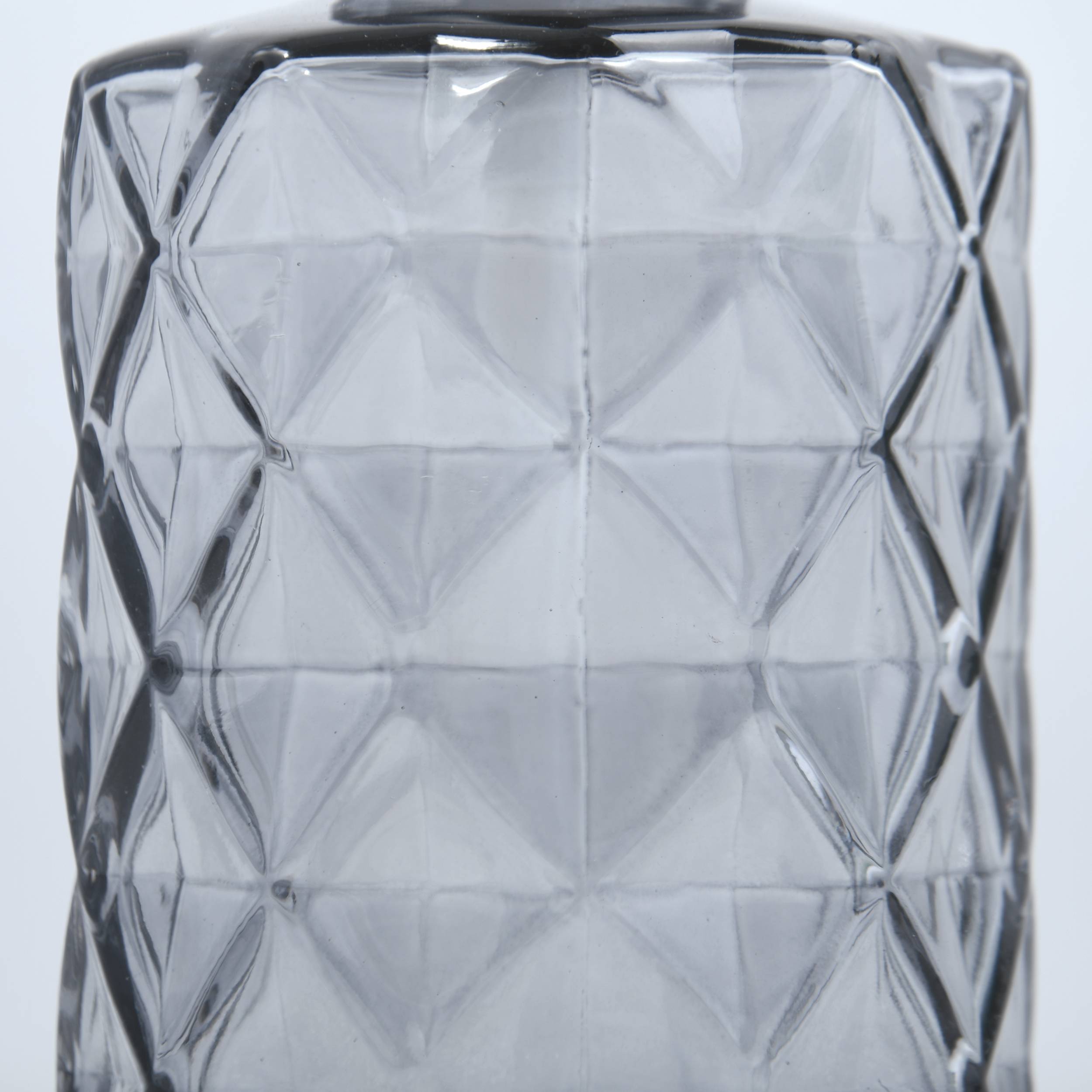 Nahaufnahme eines klaren, facettierten Glastumbler oder einer Vase mit einem geometrischen Rautenmuster vor einem einfachen, hellen Hintergrund.