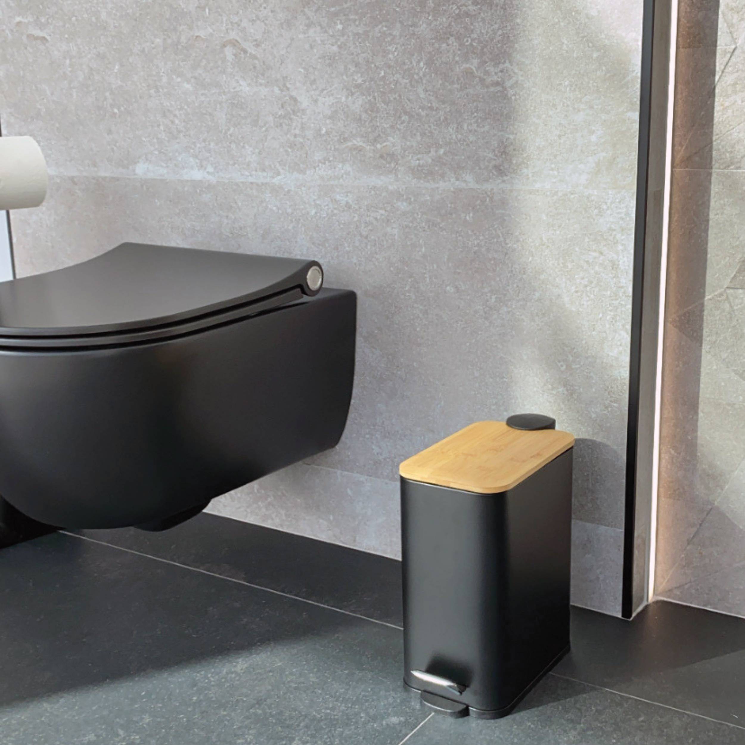 Modernes Badezimmer mit einer wandmontierten schwarzen Toilette und einem passenden schwarzen Treteimer mit Holzdeckel und Fußpedal.