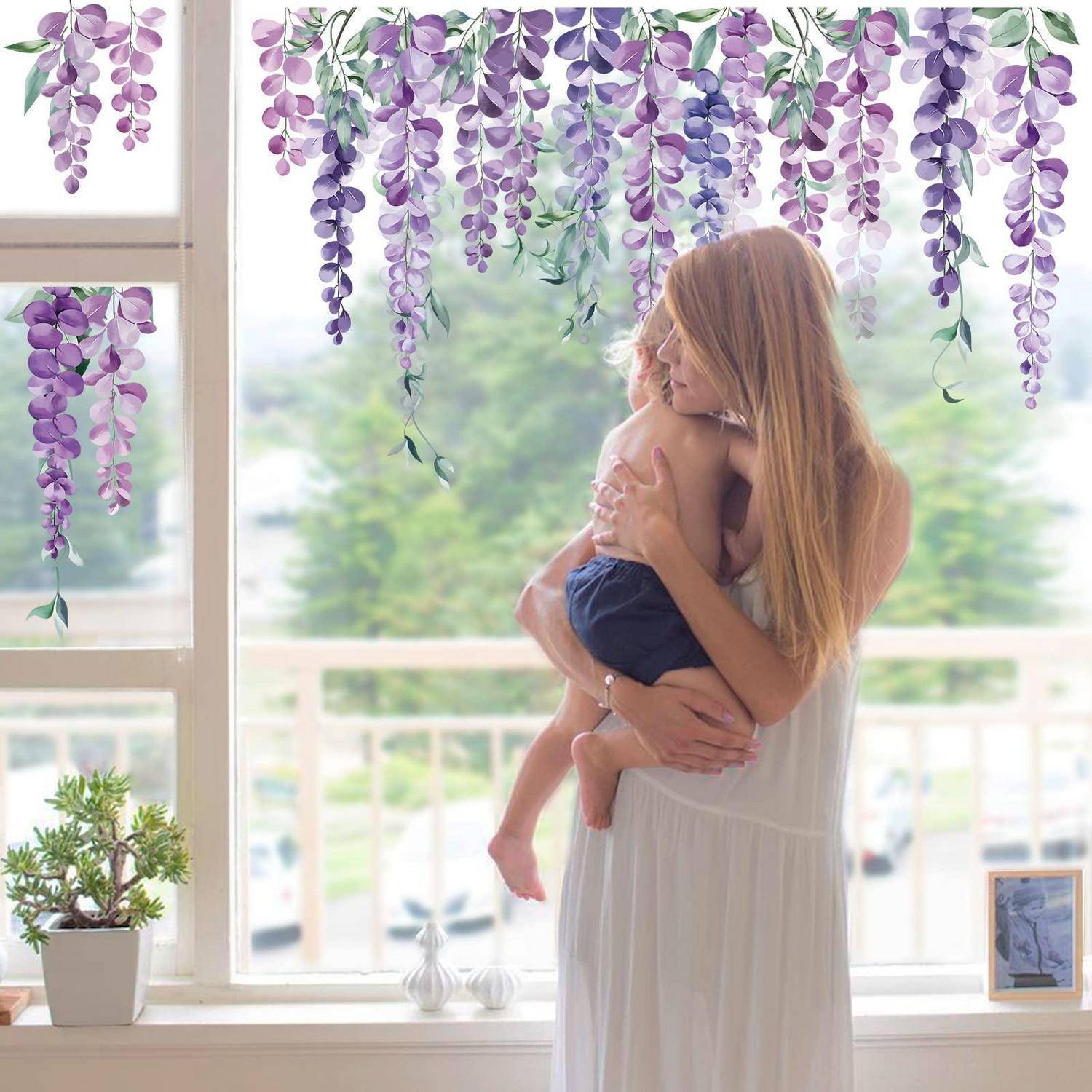 Frau in einem weißen Kleid, die ein kleines Kind an einem hellen Fenster hält und tröstet, mit hängenden violetten Blumen oben darüber.