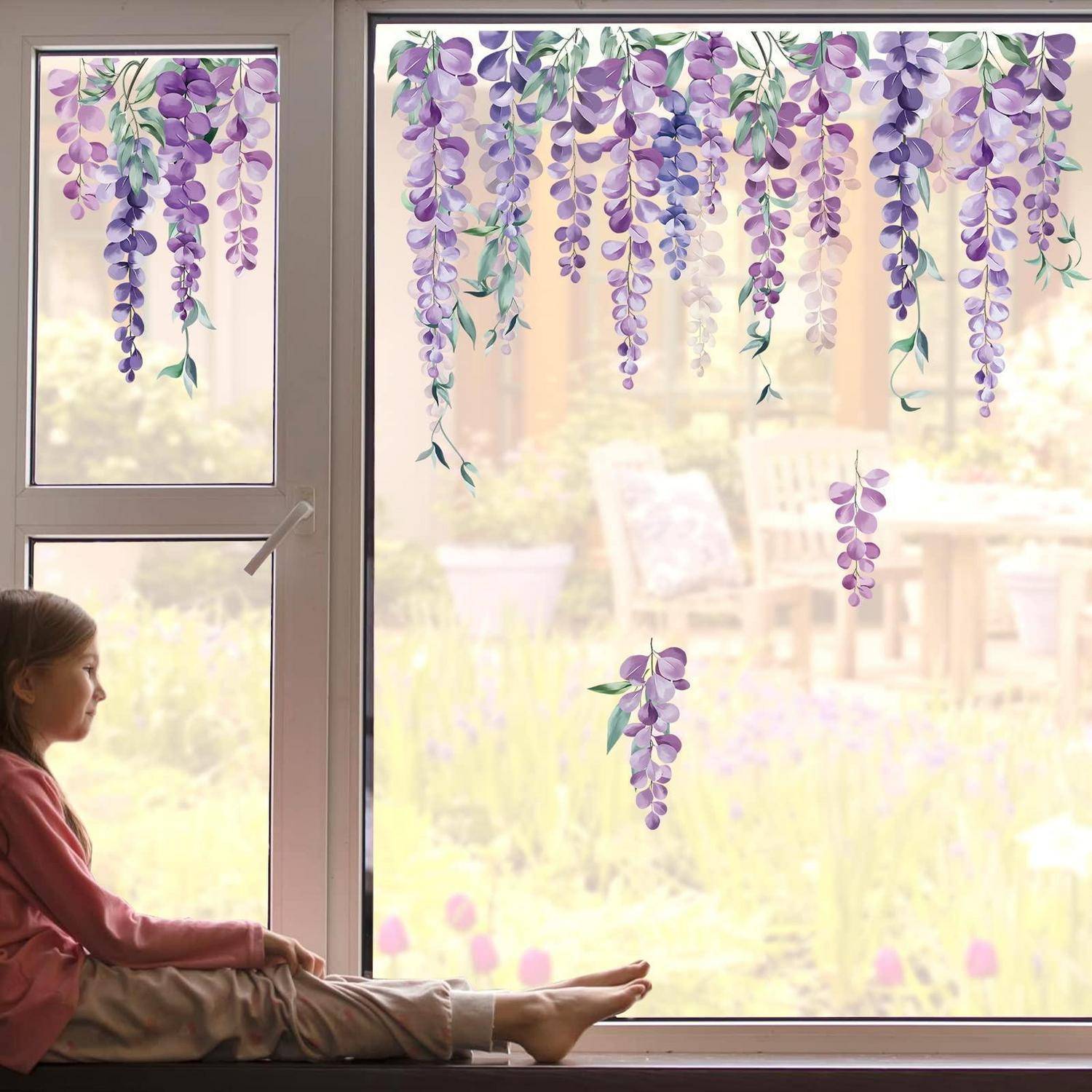Mädchen, das auf einer Fensterbank sitzt und durch ein helles Fenster schaut, das mit hängenden violetten Glyzininenblüten geschmückt ist.