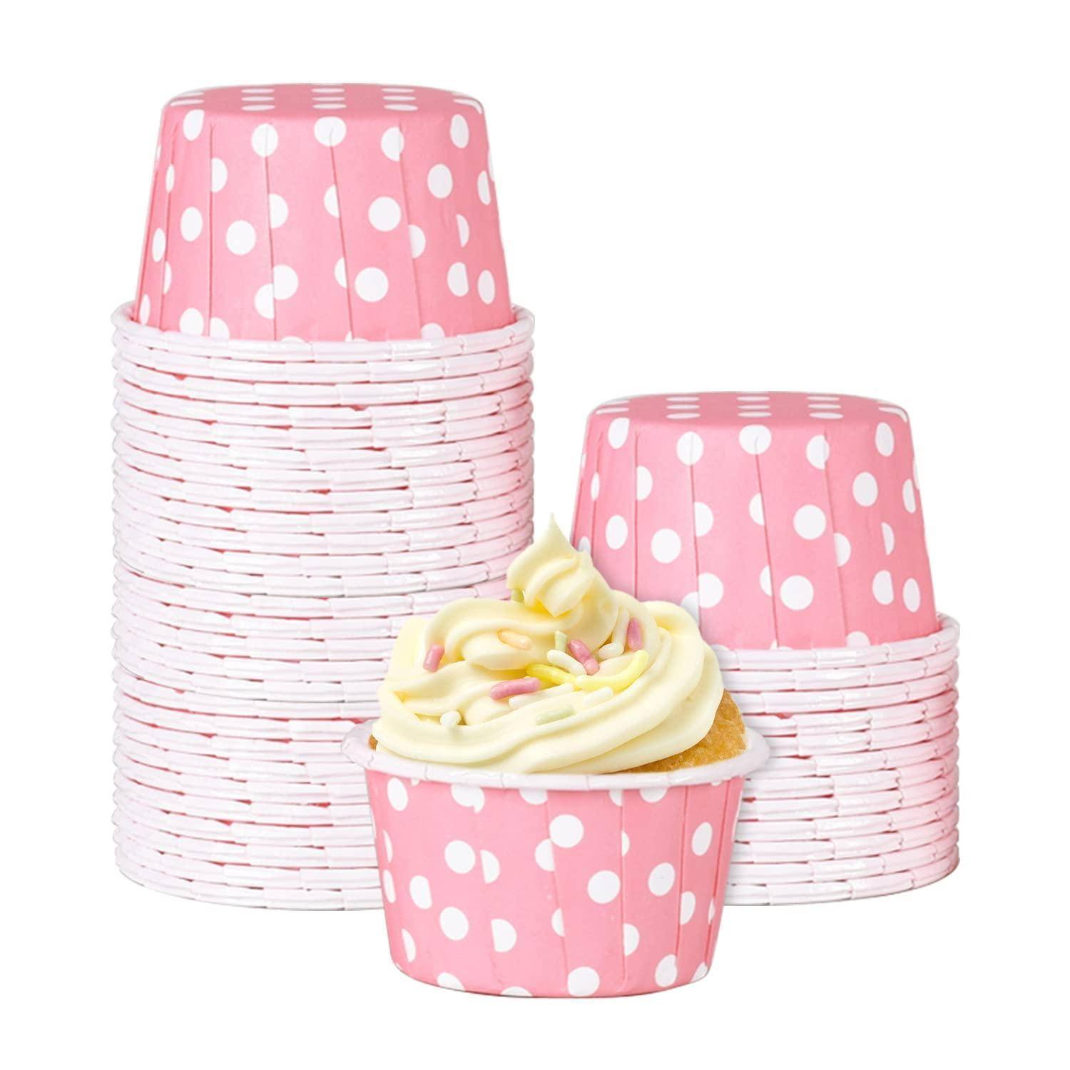 Gestapelte rosa Cupcake-Förmchen mit weißen Punkten und ein glasierter Cupcake davor auf weißem Hintergrund.