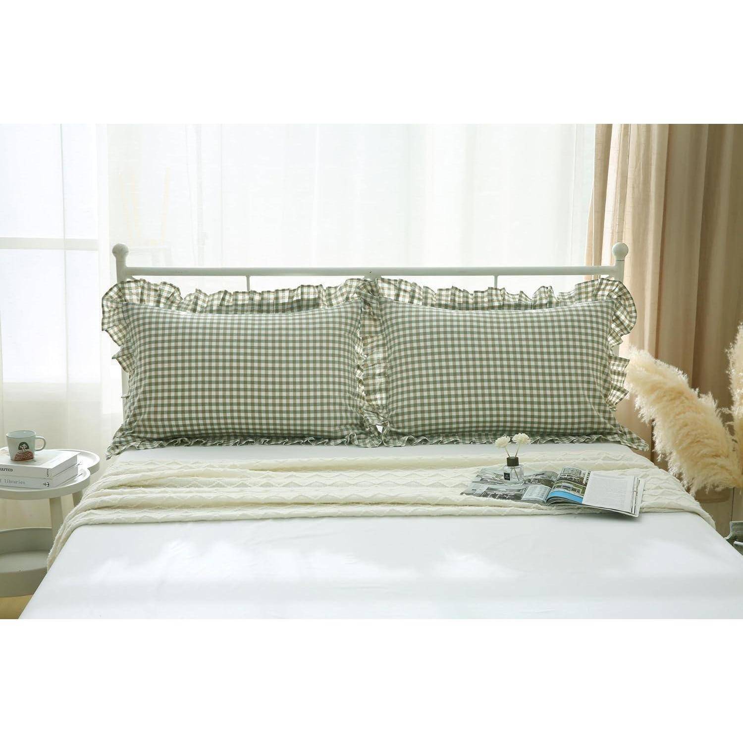 Ein sauber gemachtes Bett mit grünen Gingham-Rüschen-Kissen, einer weißen Steppdecke und einem aufgeschlagenen Buch bei einem sonnigen Fenster.