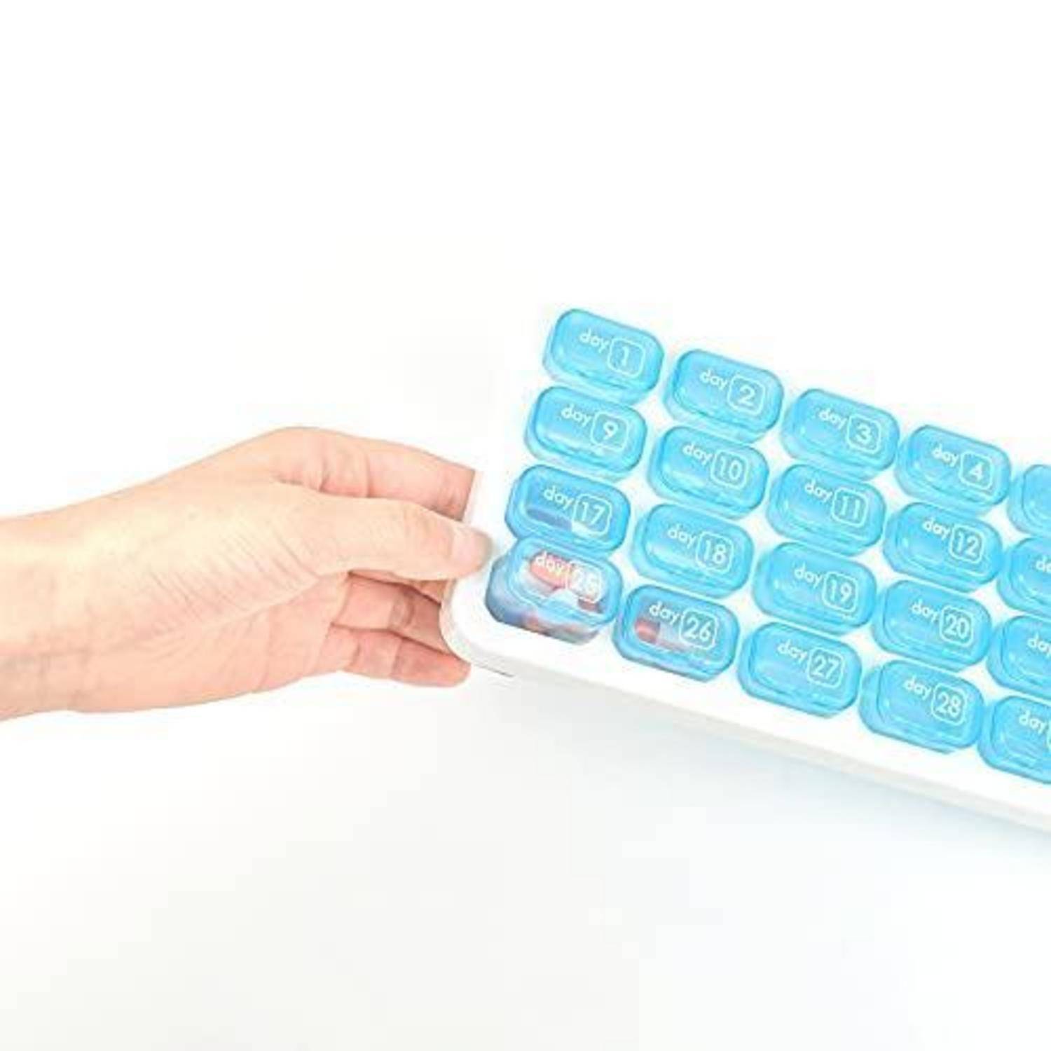 Eine Hand hält ein kleines weißes Tablett mit blauen, nummerierten kapselförmigen Behältern, die in einem Gitter angeordnet sind.