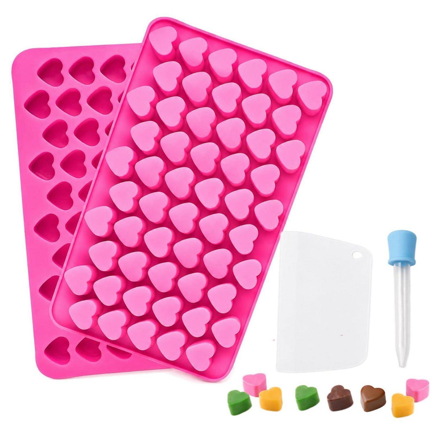 Zwei rosa herzförmige Silikonformen, ein weißer Spachtel, eine Pipette und kleine bunte herzförmige Teile auf weißem Hintergrund.