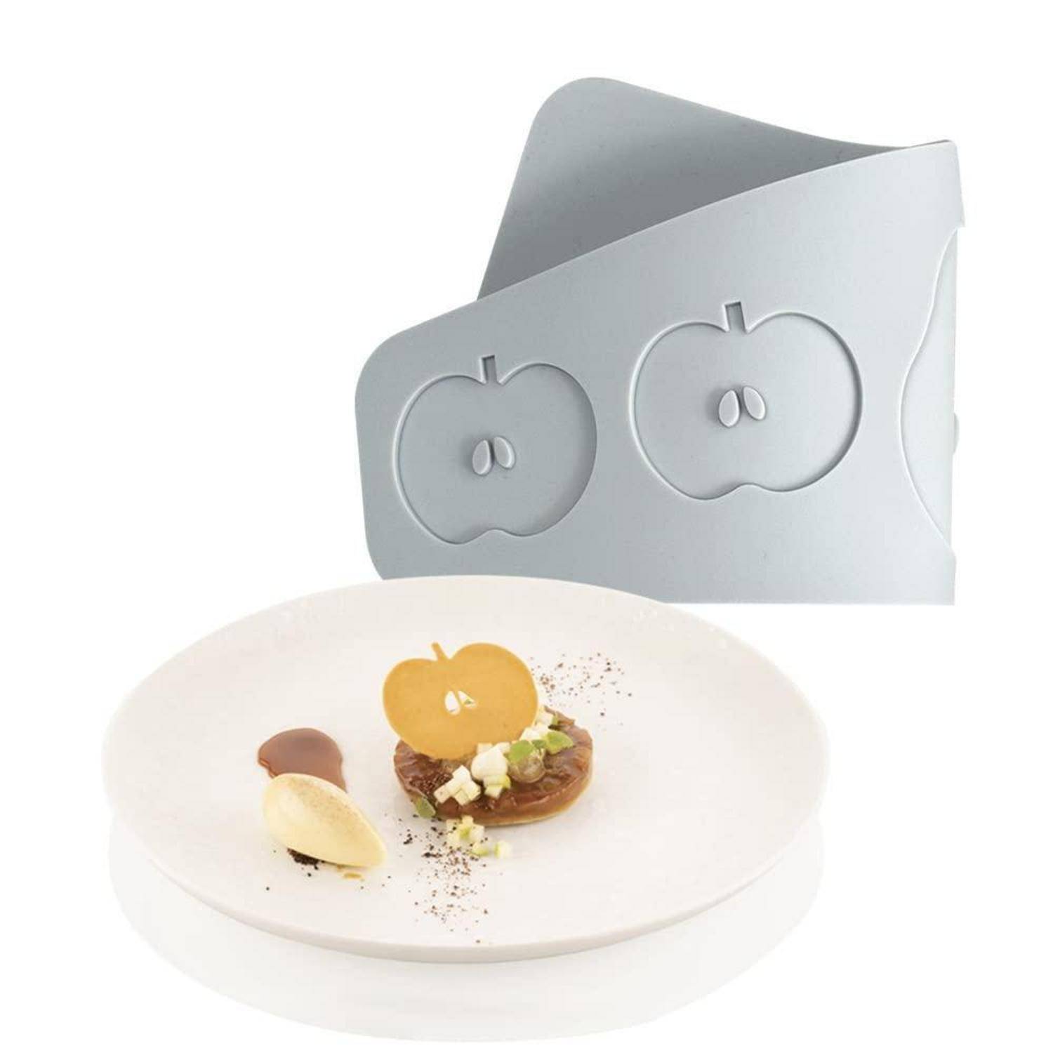 Weißer Teller mit Gourmet-Dessert, garniert mit Apfelscheiben und Krümeln, mit einer grauen apfelförmigen Form oder Verpackung darüber.