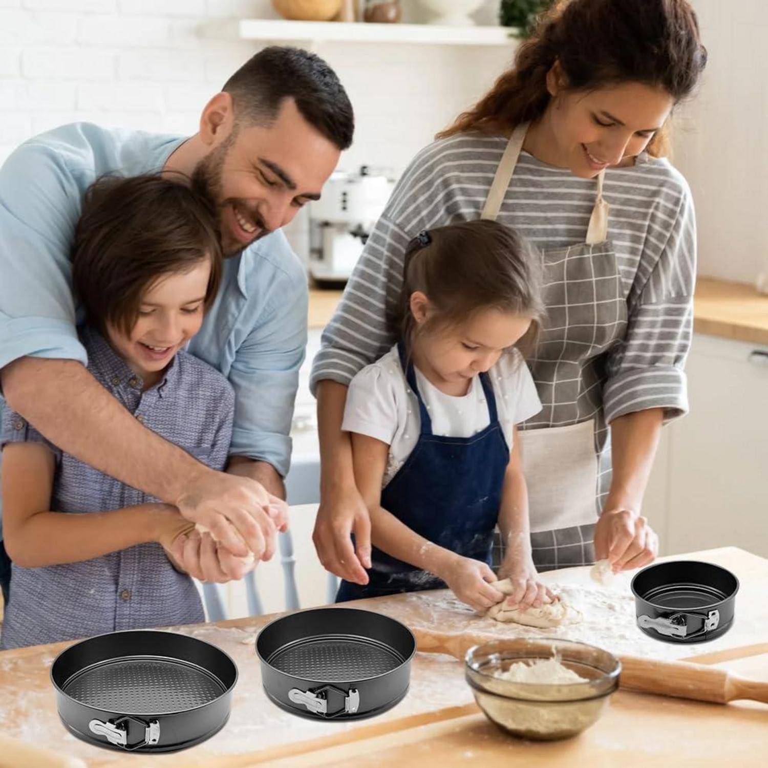 Familie von vier Personen backt zusammen in einer Küche, rollt Teig auf einer bemehlten Arbeitsfläche aus, während Kuchenformen und eine Schüssel mit Teig in der Nähe stehen.