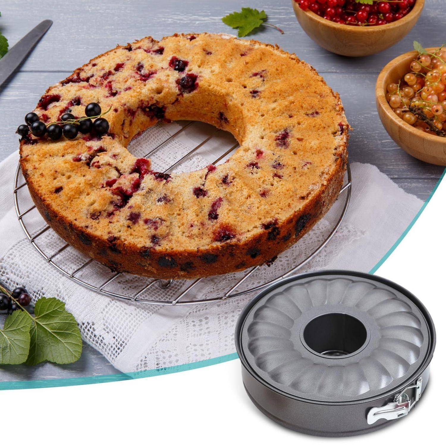 Beeren-Gugelhupf auf einem Abkühlgitter, daneben eine Antihaft-Gugelhupfform und Schalen mit Beeren im Hintergrund.