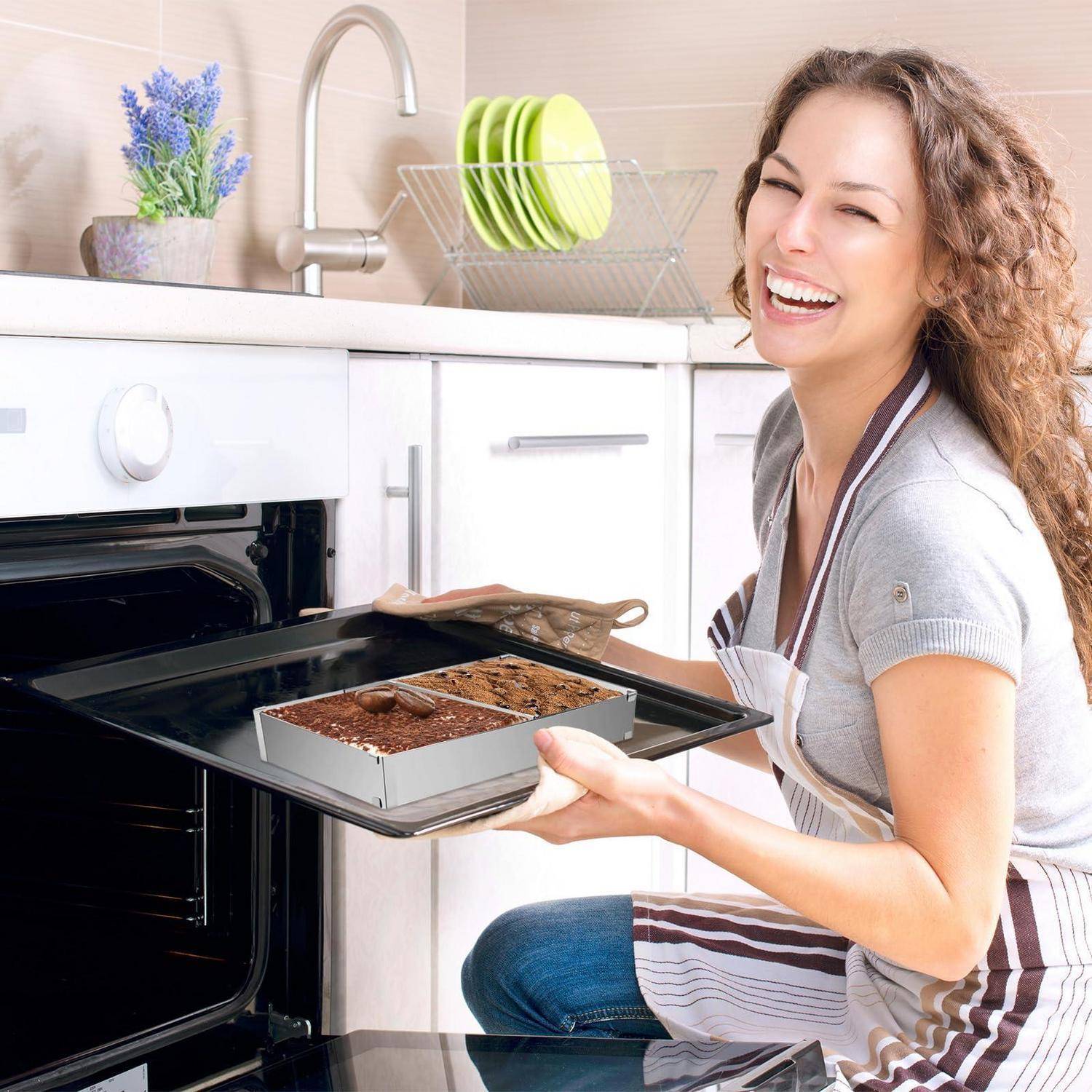 Lächelnde Frau in einer Schürze nimmt einen frisch gebackenen Kuchen aus einem Ofen in einer hellen Küche.
