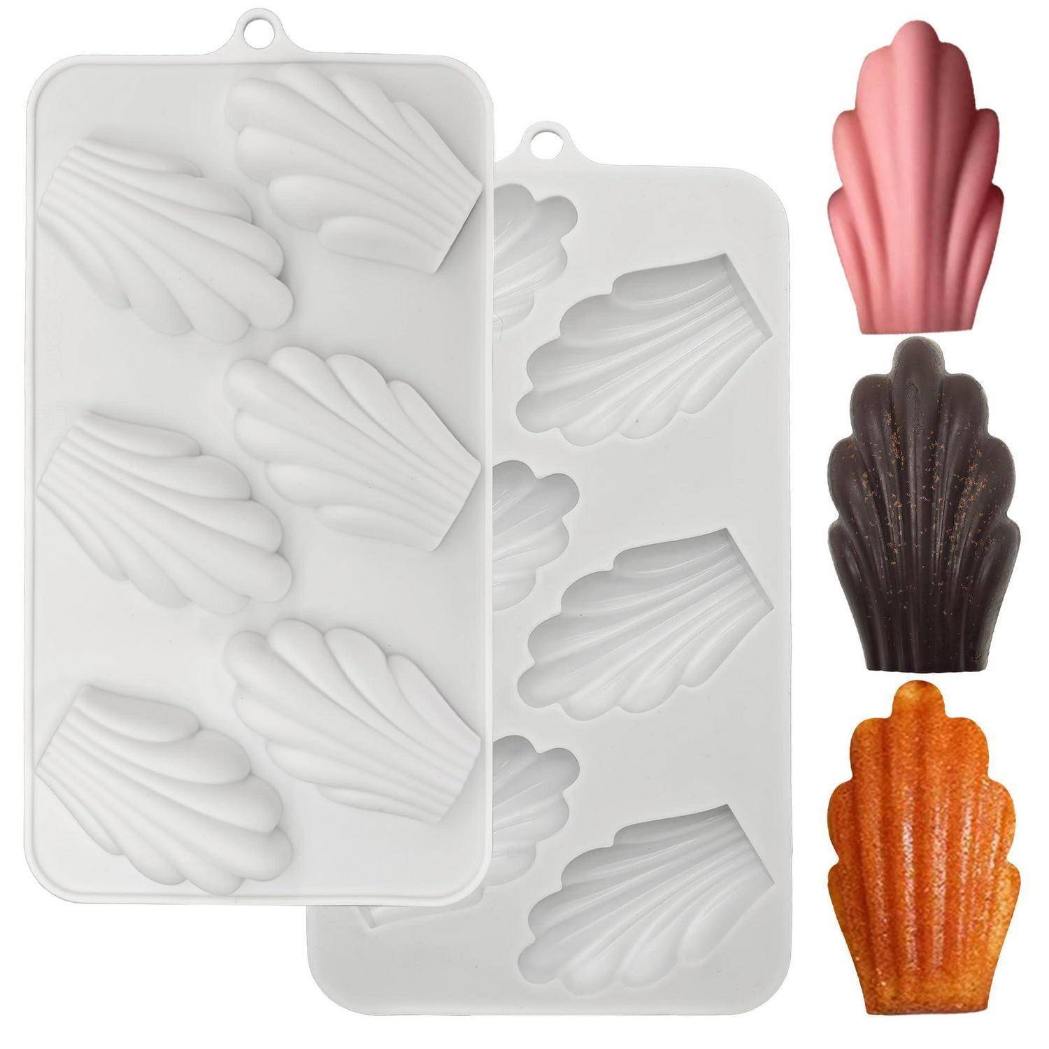 Muschelförmige Silikonformen in Weiß, gezeigt mit drei fertigen Madeleines in Rosa, Dunkelbraun und Orange.