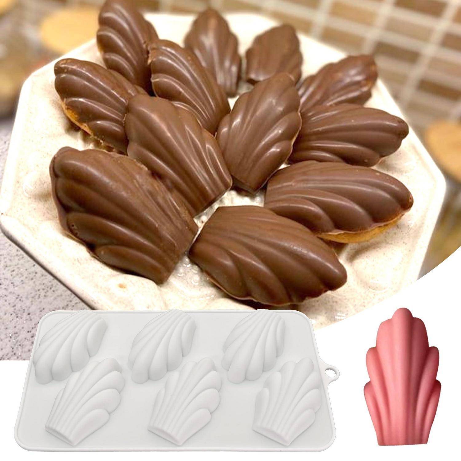 Madeleines mit Schokoladenhülle auf einem Teller angeordnet, mit einer Madeleine-förmigen Form und einer rosa muschelförmigen Süßwarenform unten abgebildet.