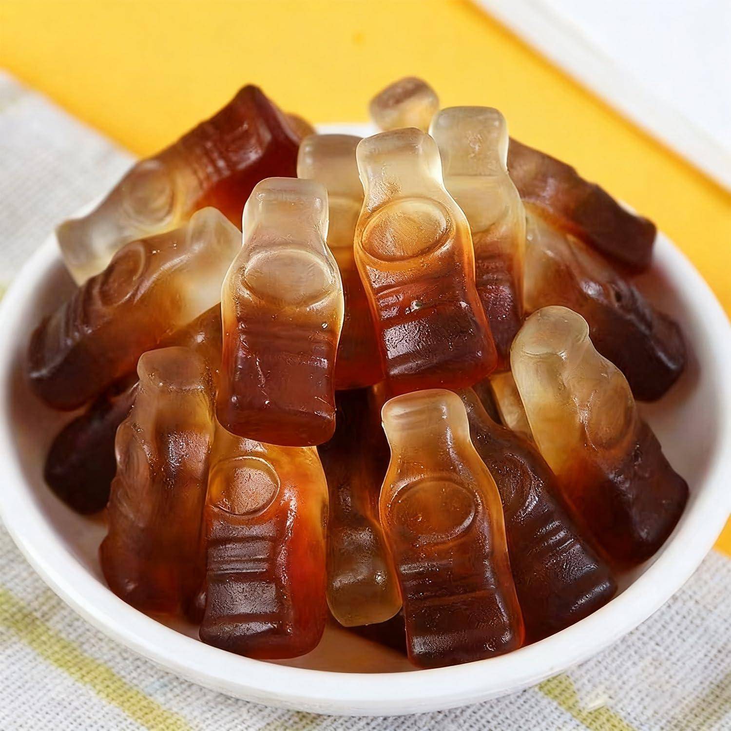 Schüssel mit cola-flaschenförmigen Gummibonbons, die auf einem gelb gestreiften Tuch übereinander gestapelt sind.