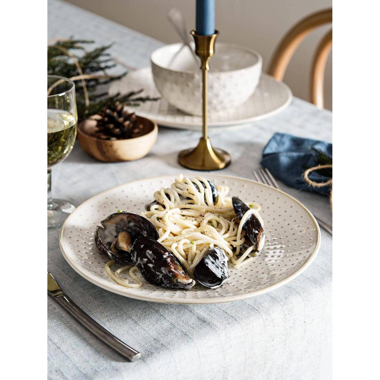 Teller mit Spaghetti und Muscheln auf einem Esstisch, mit einem Glas Wein und Kerzen im Hintergrund.