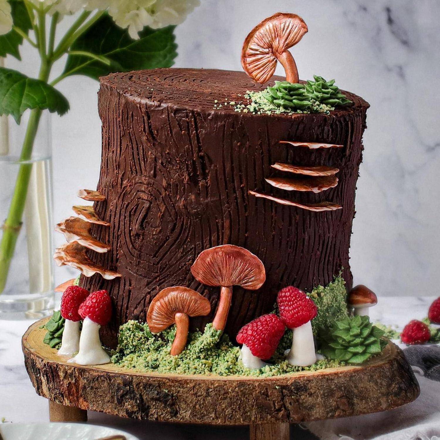 Ein waldthematiger Schokoladenkuchen, dekoriert wie ein Baumstumpf mit Pilzen, Himbeeren und Grünzeug auf einem Holzständer.