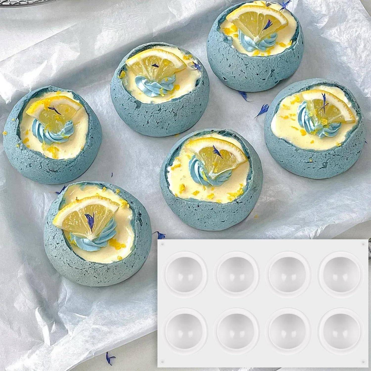 Sechs blaue muschelförmige Zitronendesserts mit Creme und Garnitur auf Pergamentpapier, gezeigt mit einer weißen Förmchen-Form für sechs Portionen.