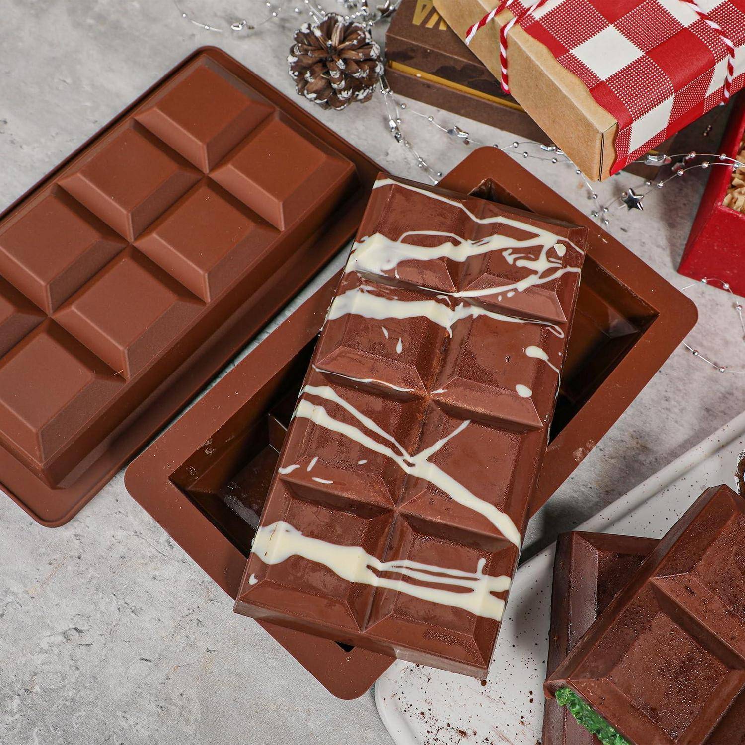 Assortierte Schokoladentafeln in braunen Kunststoffformen, darunter Milch- und weiß gespritzte Schokolade, mit Geschenkboxen und Weihnachtsdekoration in der Nähe.