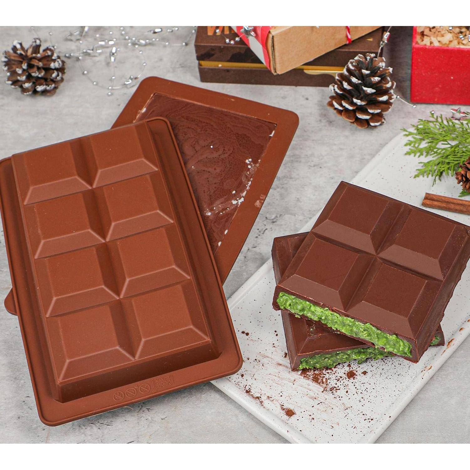 Schokoladenform mit geschmolzener Schokolade; rechts ein fertiggestellter Schokoriegel gefüllt mit grüner Creme auf einem weißen Tablett, mit Tannenzapfen und Geschenkboxen im Hintergrund.