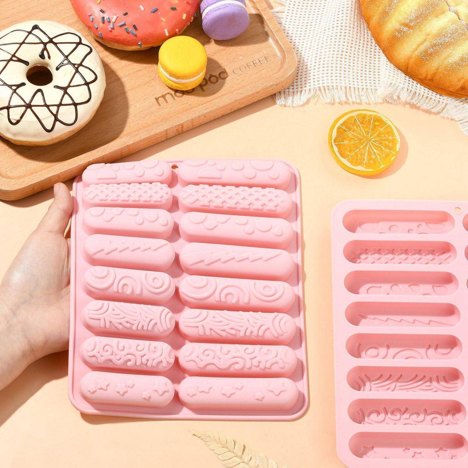 Hand, die ein rosa Silikonform-Tablett mit assotierten dekorativen Stäbchenformen auf einem Pastell-Dessert-Thema-Hintergrund mit Donuts und Makronen hält.