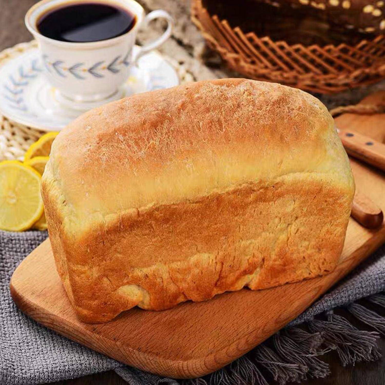 Laib frisch gebackenes Brot auf einem Holzbrett mit einer Tasse Kaffee und Zitronenscheiben im Hintergrund.