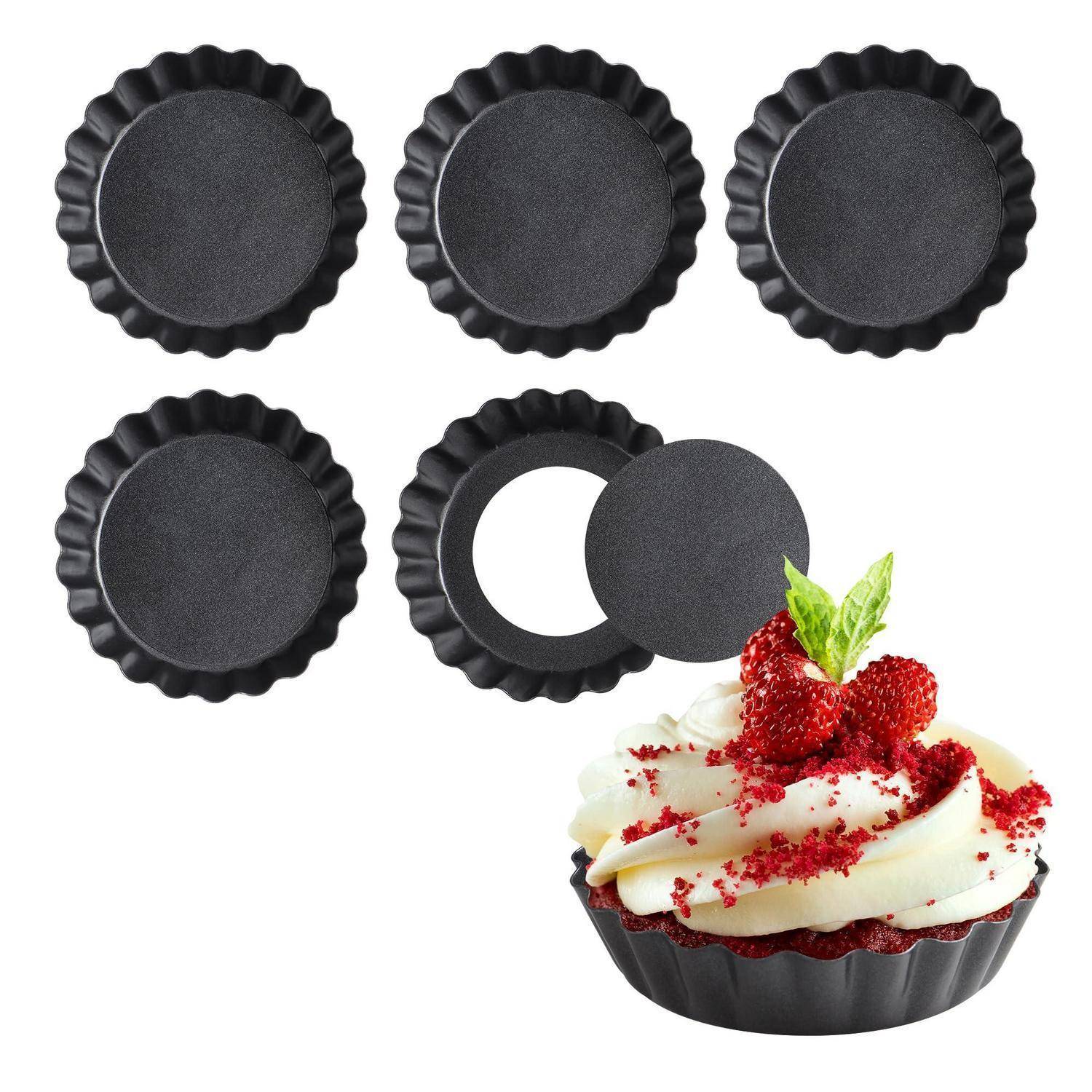 Satz schwarzer gerippter Mini-Tarteformen mit einer offenen Form, daneben eine fertige mit Obst belegte Tarte in einer Form.
