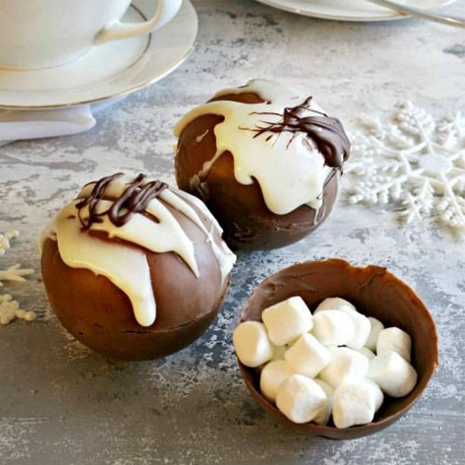 Schokoladen-Dessert-Kugeln mit weißer und dunkler Schokolade beträufelt, neben einer kleinen Schüssel voller Marshmallows auf einem Tisch.