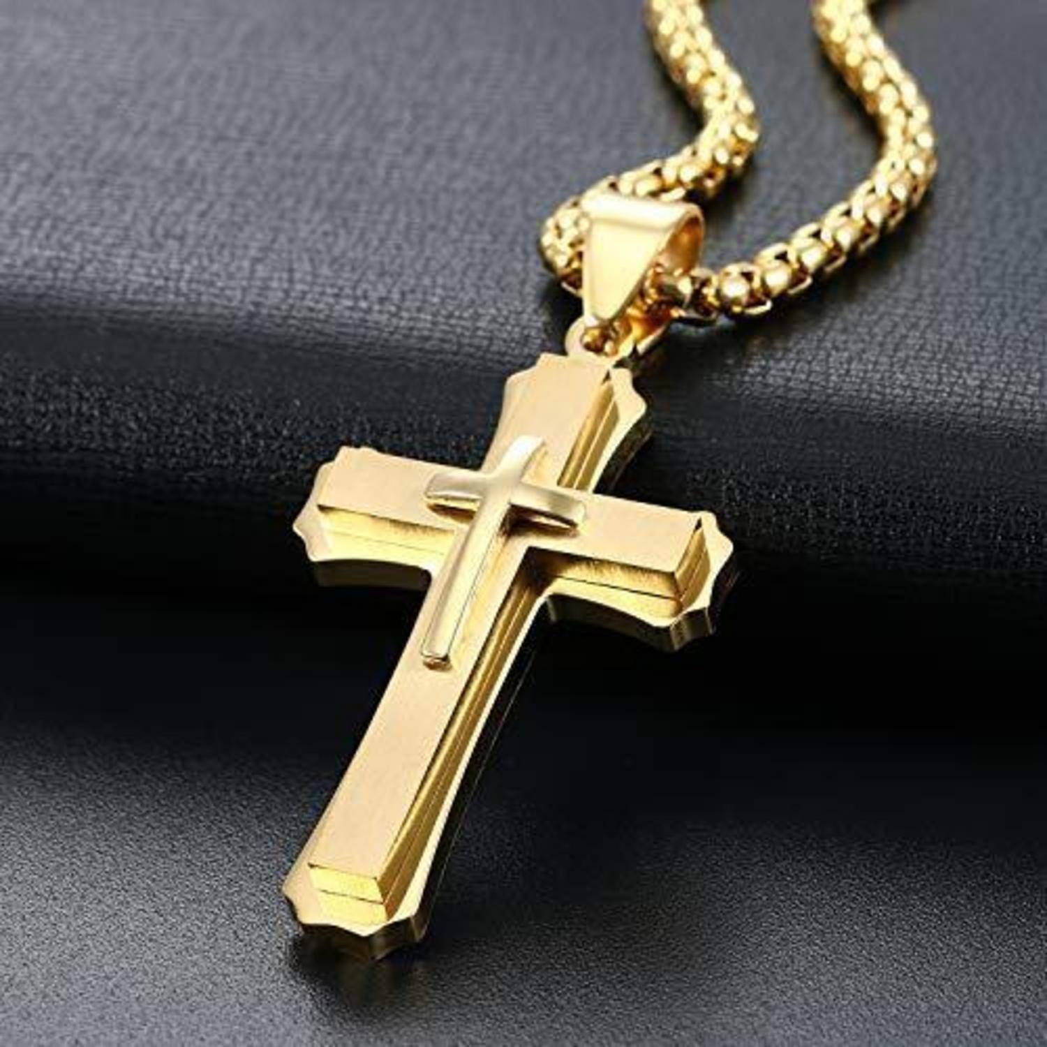 Goldenes Kreuzanhänger-Collier an einer Kette, gezeigt vor einem dunklen strukturierten Hintergrund.