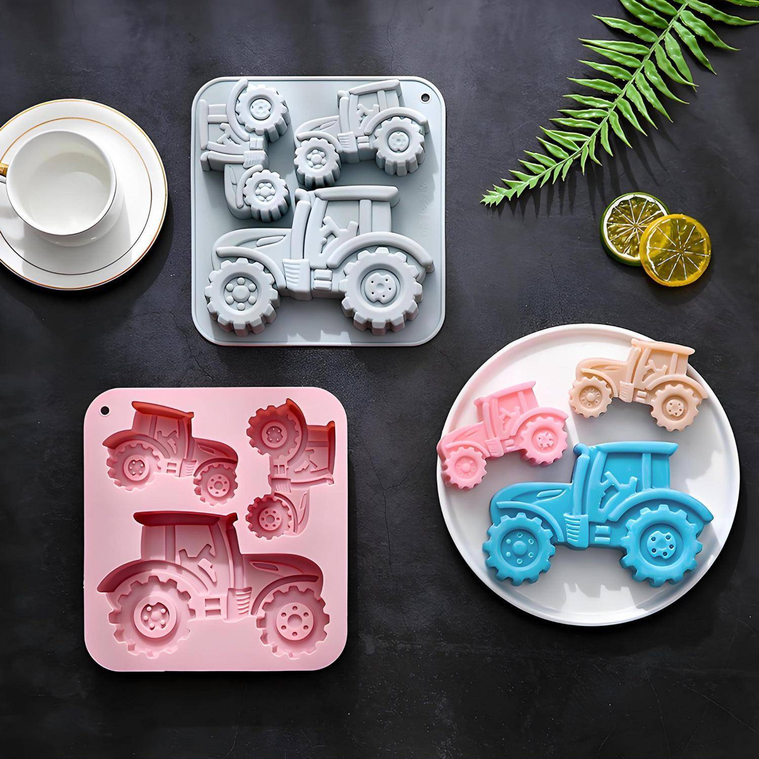 Drei Teller mit traktorförmigen Keksen oder Seifen in Grau, Rosa und gemischten Farben auf einer dunklen Tischplatte angeordnet mit einer Tasse und dekorativen Blättern und Zitrusscheiben.